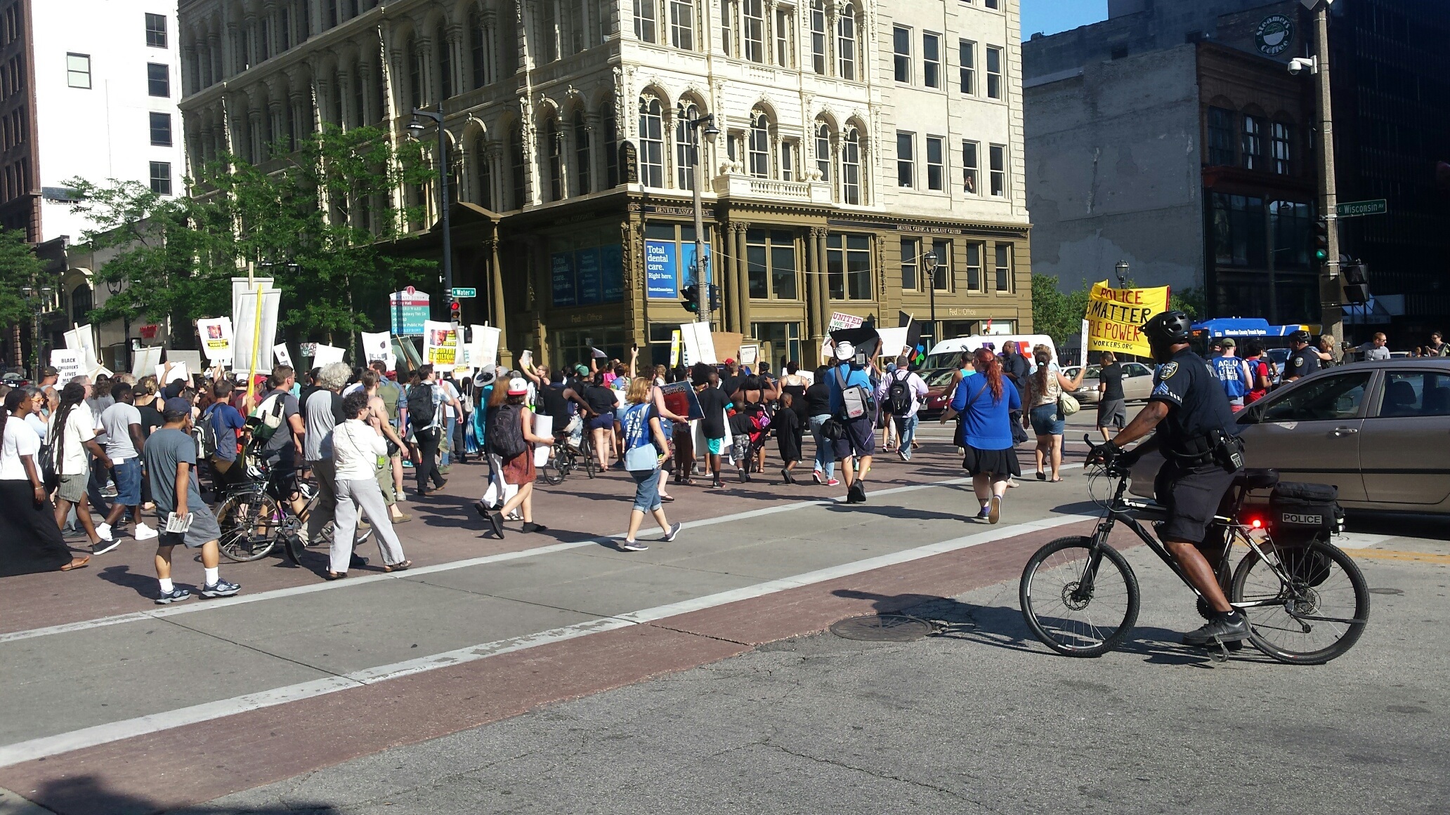 Protesters block an a intersection in downtown Milwaukee, as a police officer on a bicycle looks on.