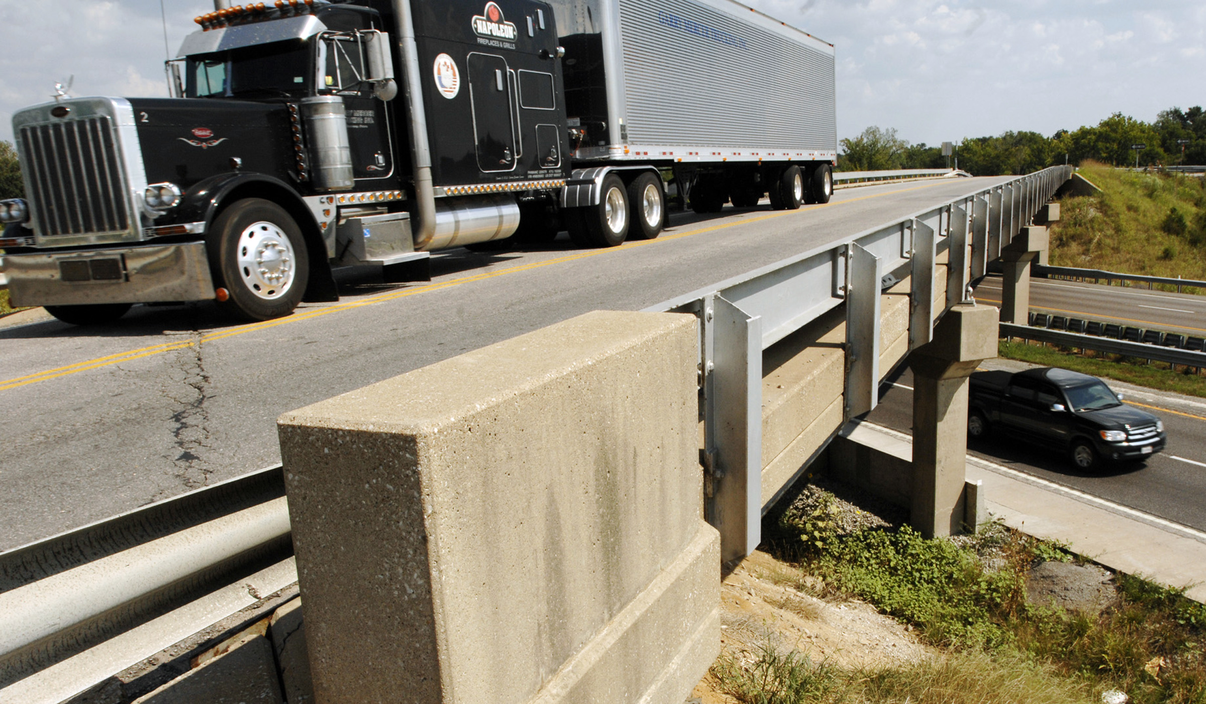 Semi-trailer truck drives on a highway bridge over an interstate