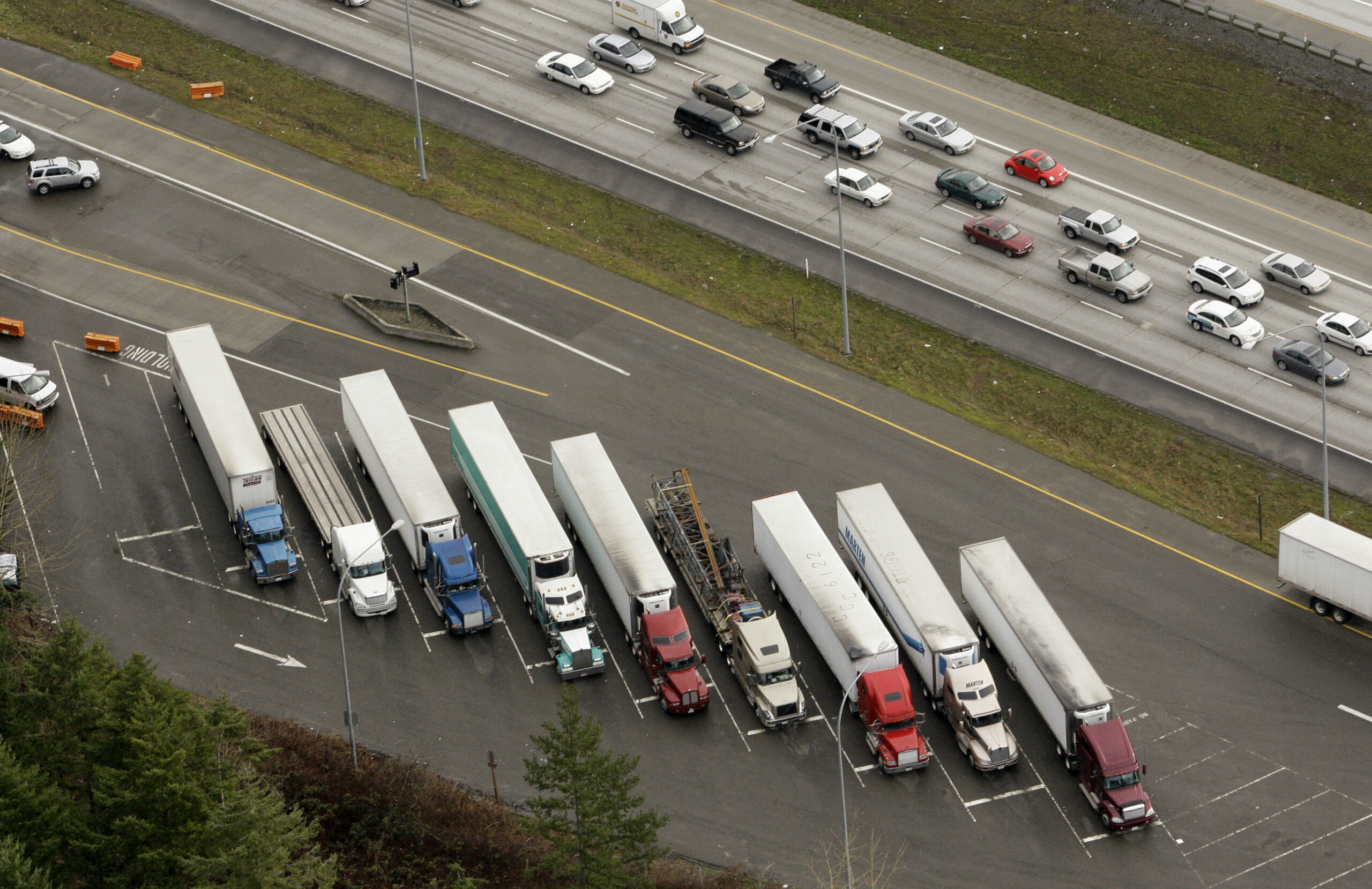Semi trailer trucks fill slots at a weigh station as traffic passes