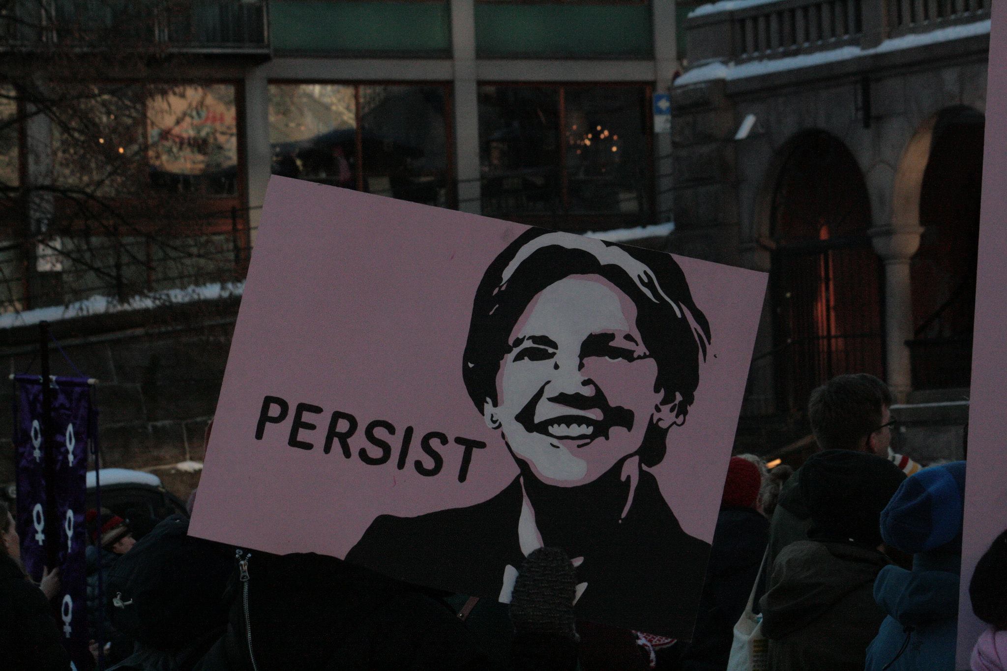 Protestors hold a sign with Senator Elizabeth Warren's image and the word "Persist" printed on it