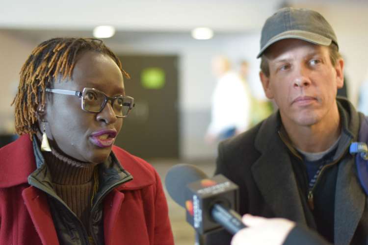 Photo of a black woman speaking earnestly into a WPR microphone while white man looks on