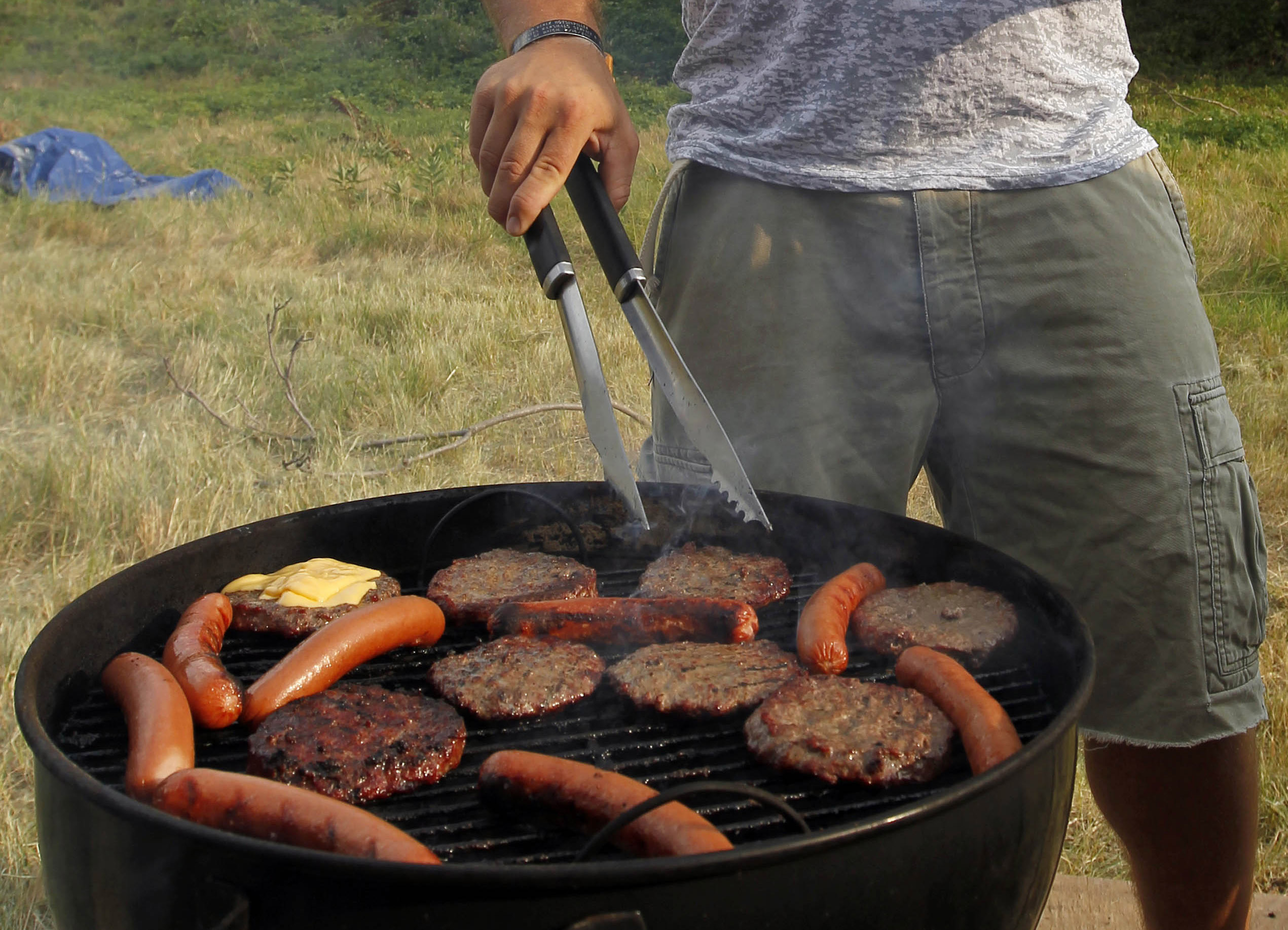 Person grilling hamburgers and hotdogs