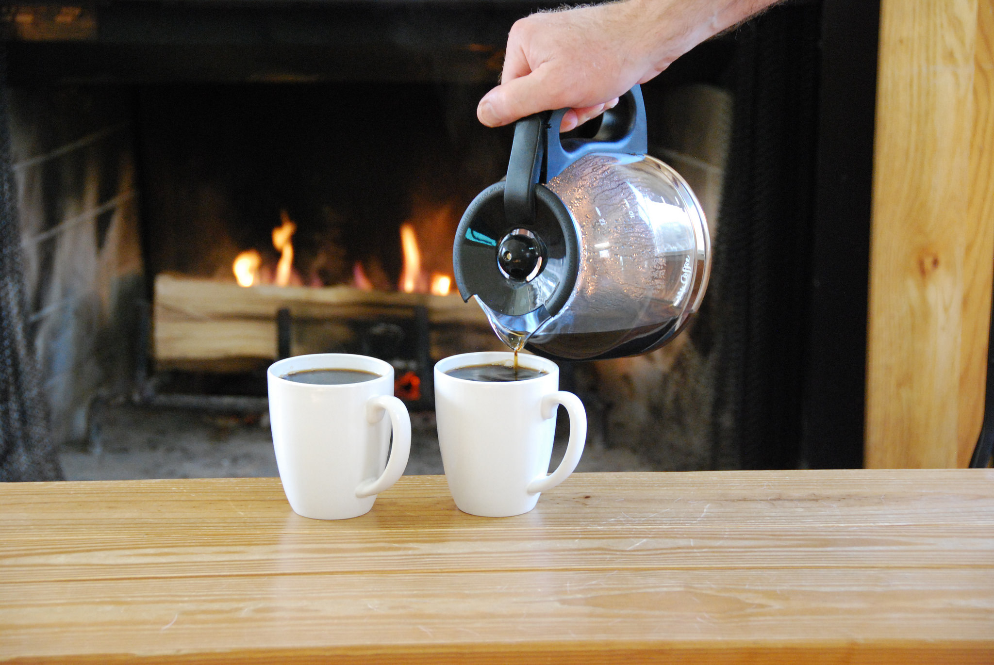 two cups of coffee being filled in front of a fireplace