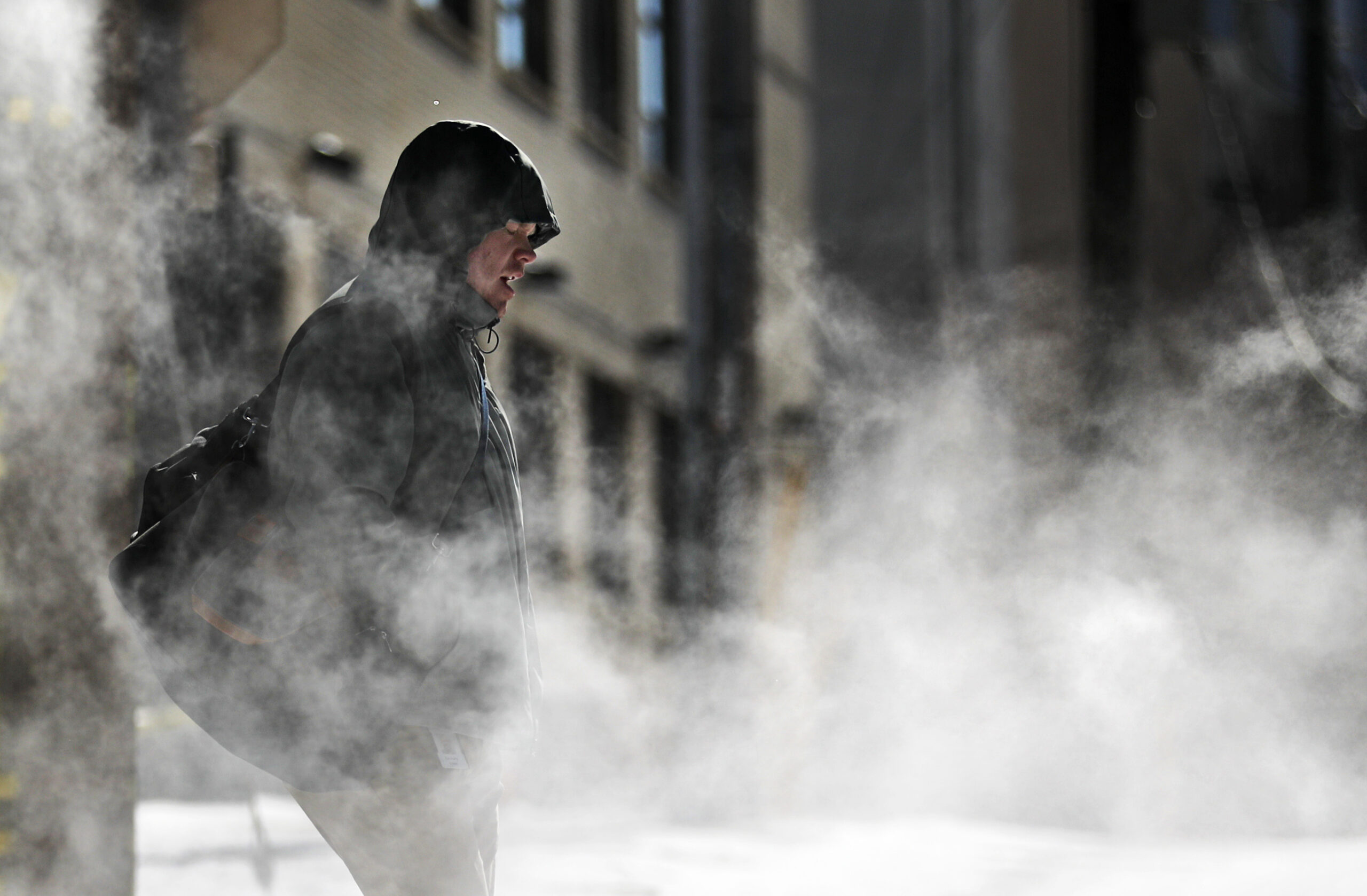 A man walks through steam venting from a building in the cold, winter weather