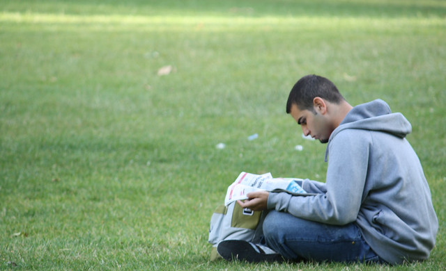 young man reading newspaper on grass