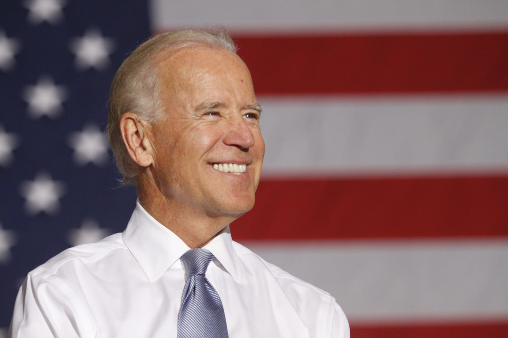 Joe Biden smiles in front of an American flag
