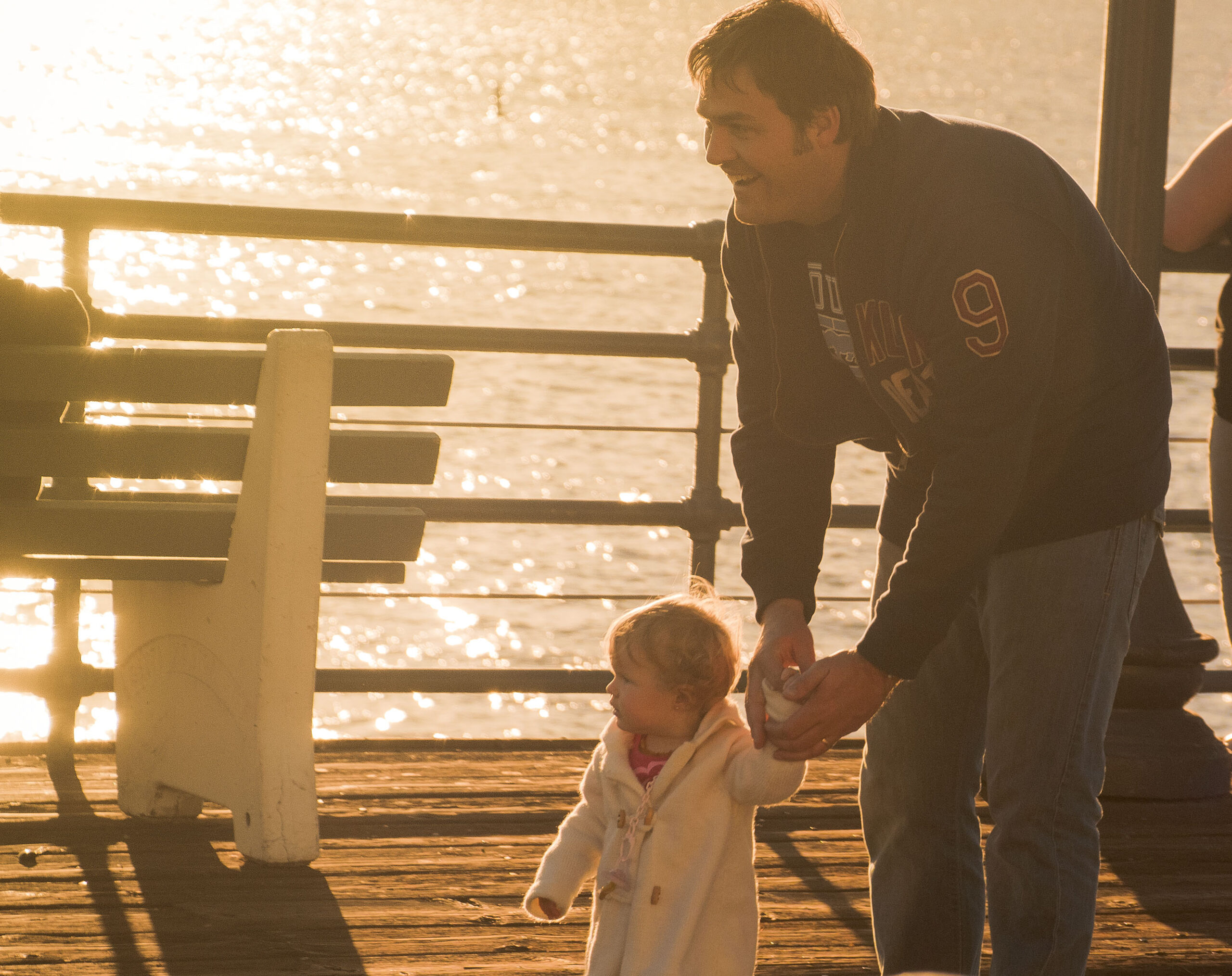 Father and toddler daughter walking on dock near water