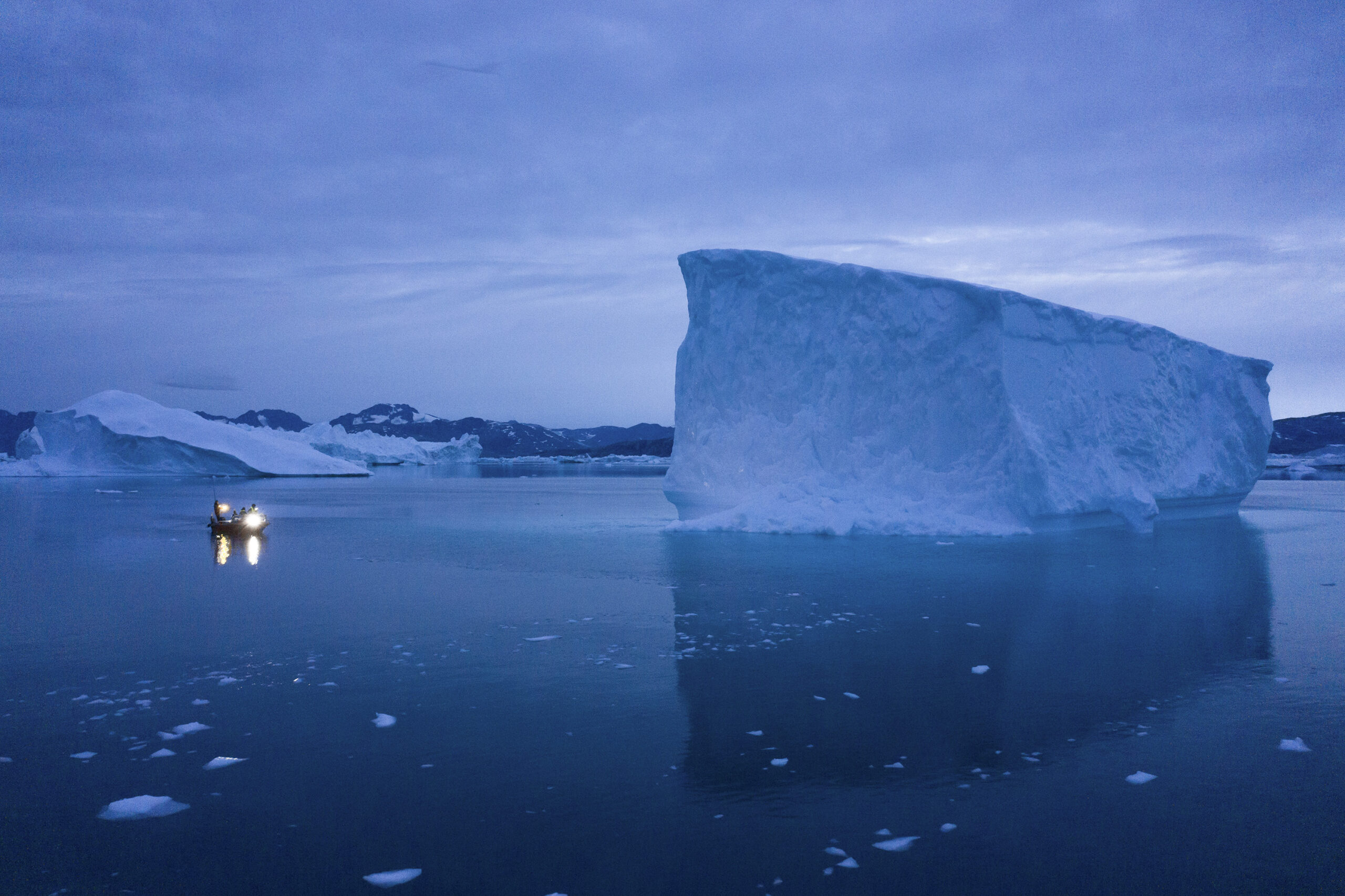 A boat navigates at night next to large icebergs in eastern Greenland.