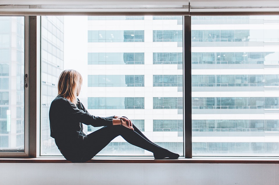 A woman sits on a ledge and looks out the window