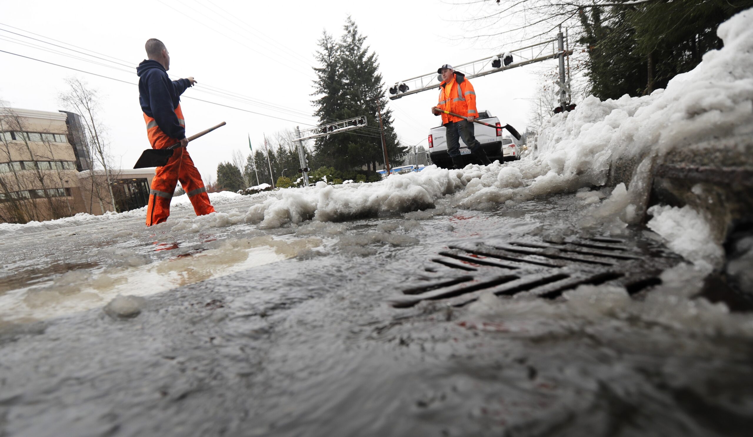 workers clear melting snow from a street drain