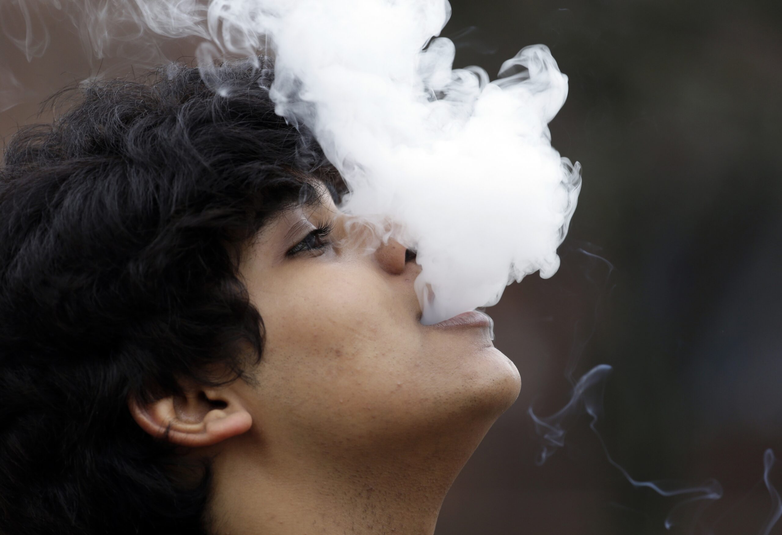man blows out a cloud of smoke from a vape pen