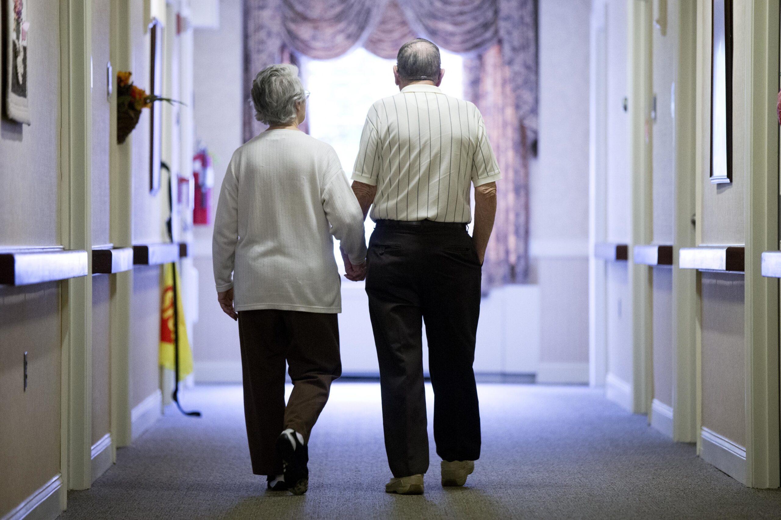 elderly couple walks down a hall of a nursing home