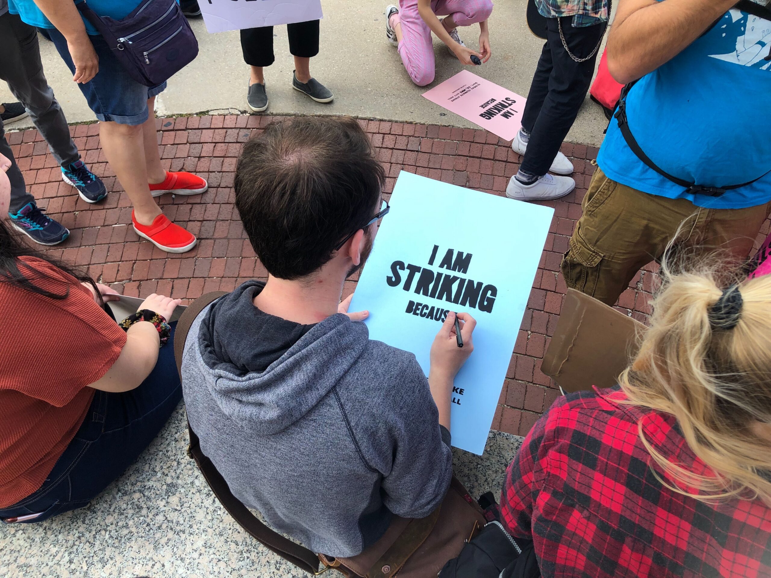 An attendee of a global climate strike rally in Milwaukee writes on a sign that says 