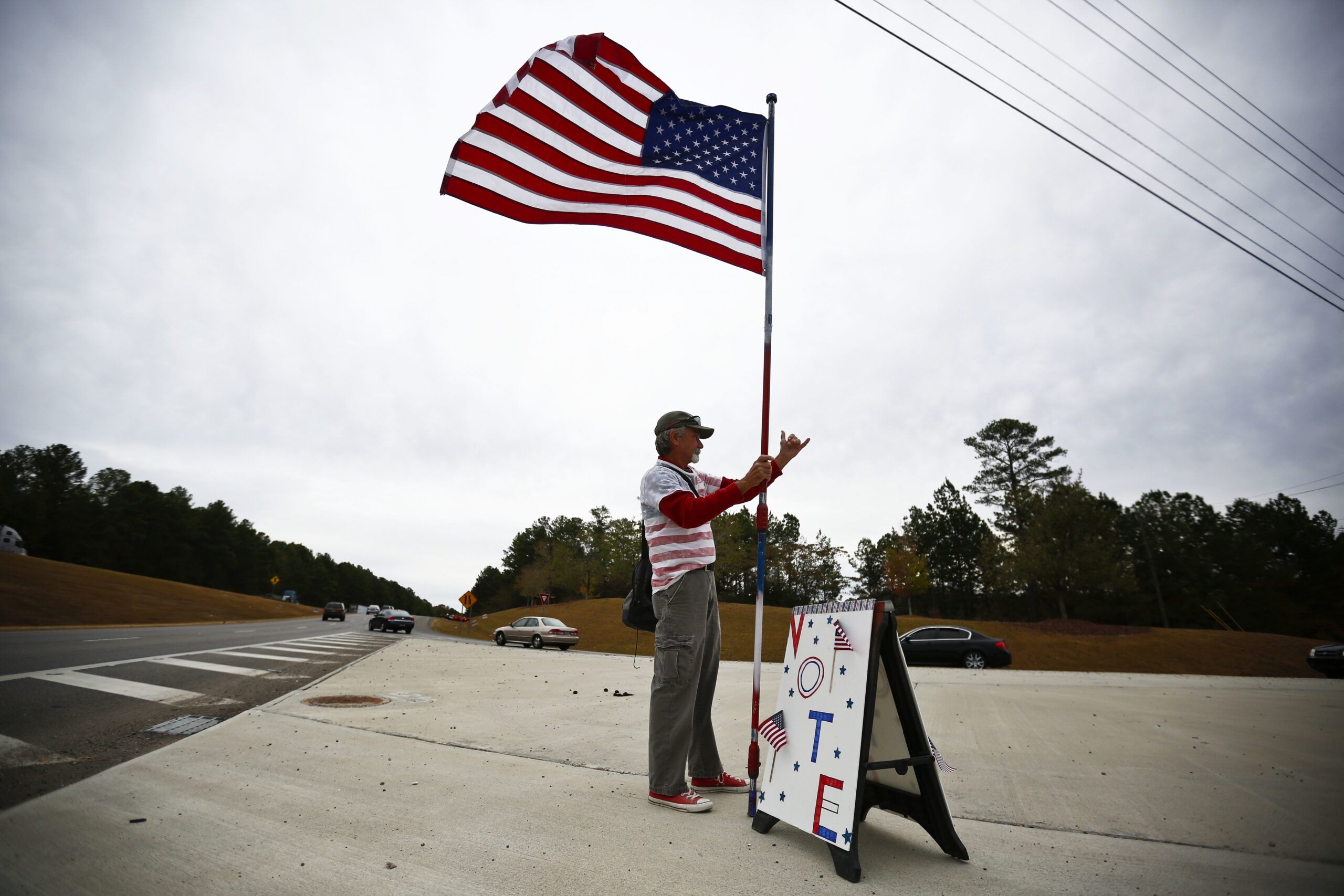 Person standing with American flag next to "vote" sign