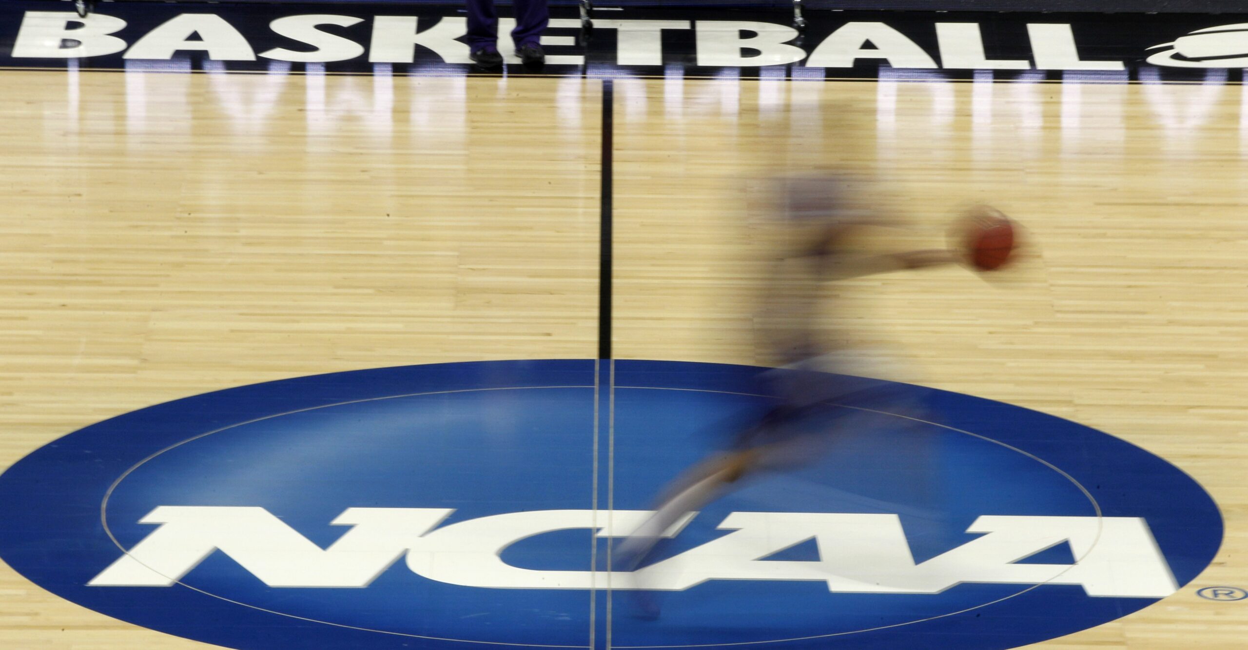 A player runs across the NCAA logo at midcourt