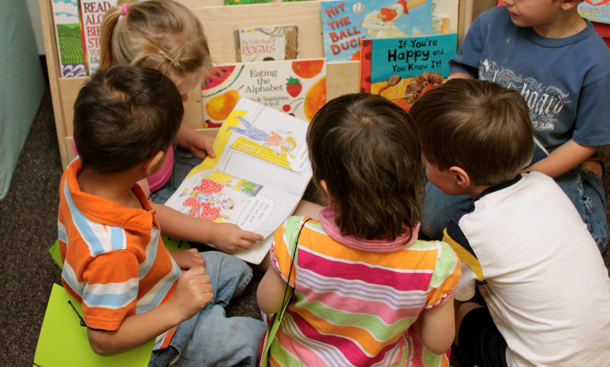 A group of children gathered around a book at child care