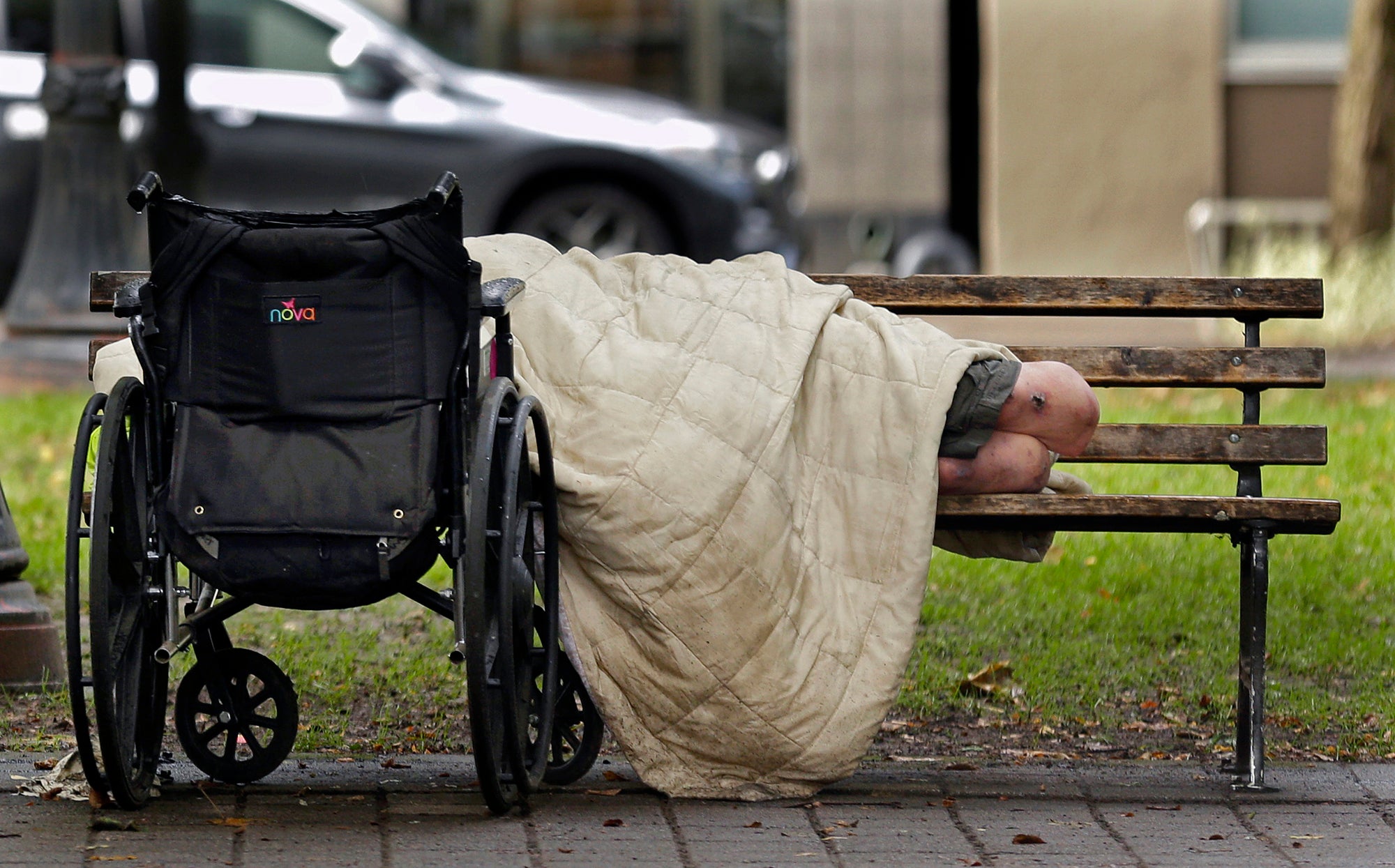 a person sleeps next to a wheelchair on a park bench
