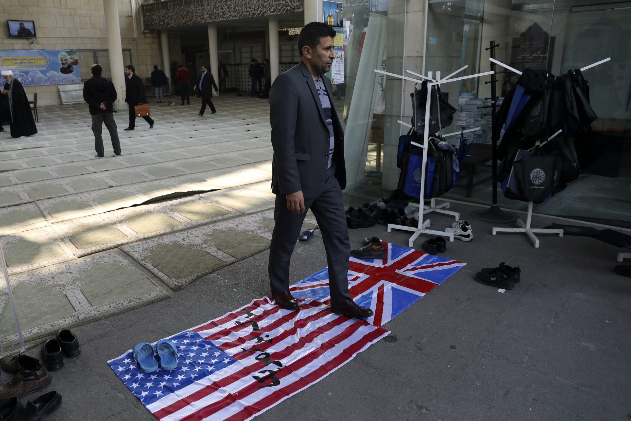 A man walks on U.S. and British flags while leaving a gathering to commemorate the late Iranian Gen. Qassem Soleimani