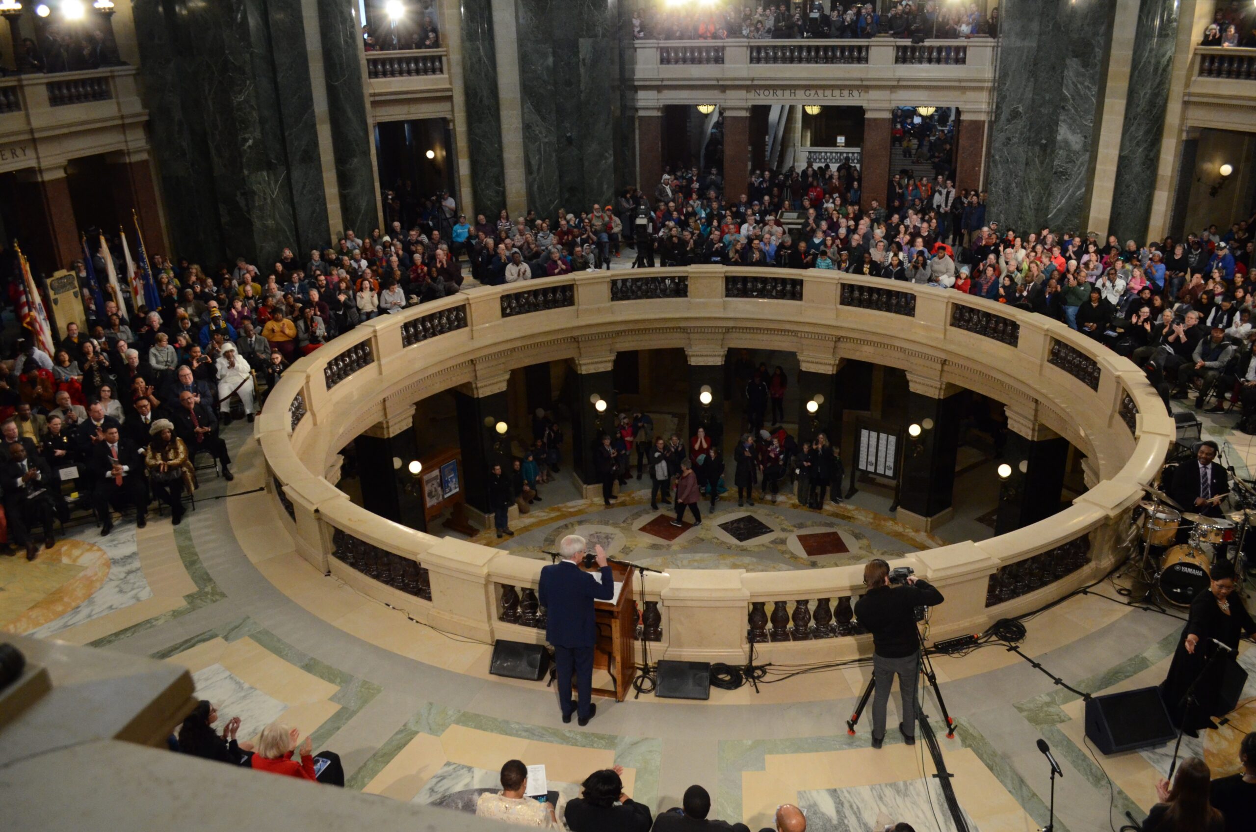 From above, you can see the governor standing at a podium. Across the balcony, hundreds of people listen.