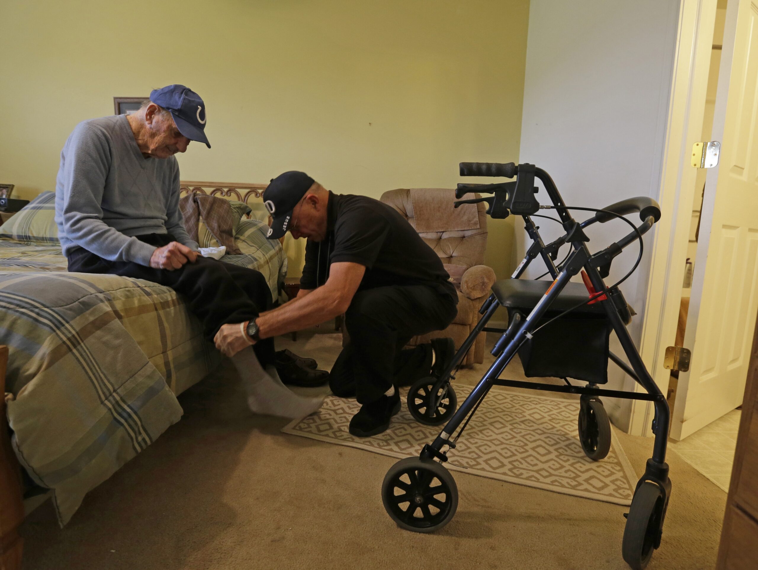 A caregiver helps an elderly man get dressed
