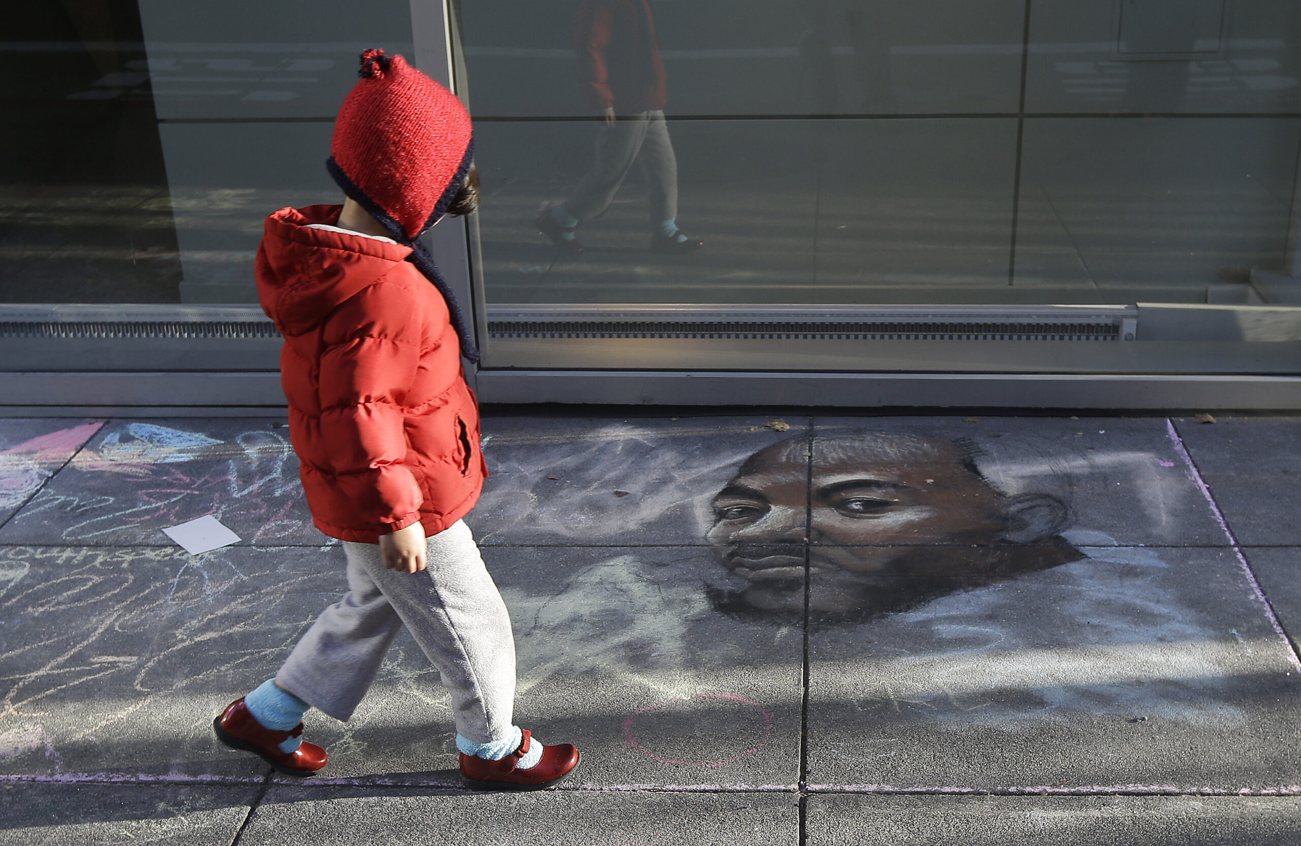 A child walks past a drawing on the sidewalk of Dr. Martin Luther King, Jr. outside of the Museum of the African Diaspora