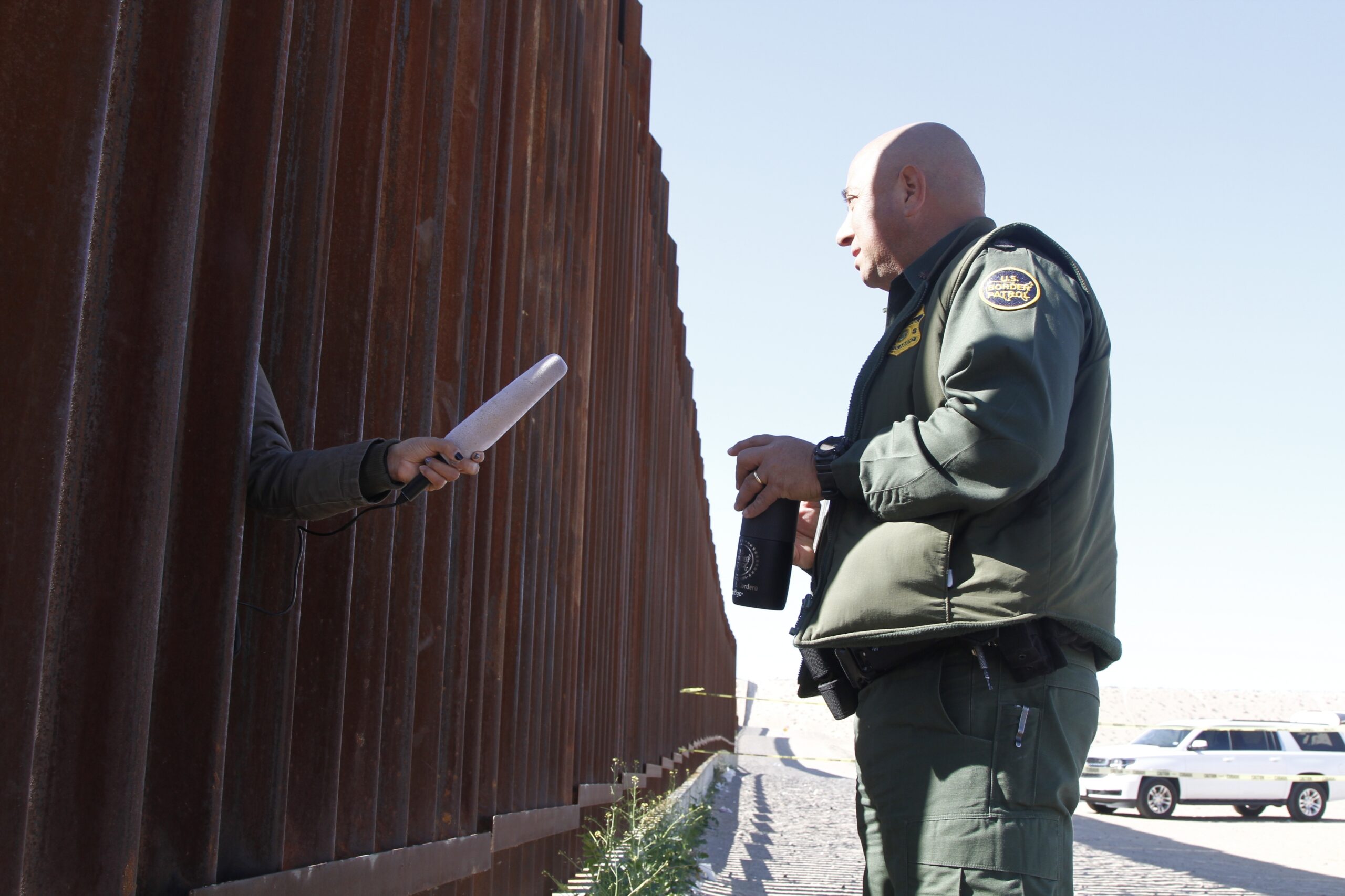 A journalist in Anapara, Mexico, sticks her microphone through a through a border fence to interview a Border Patrol agent.