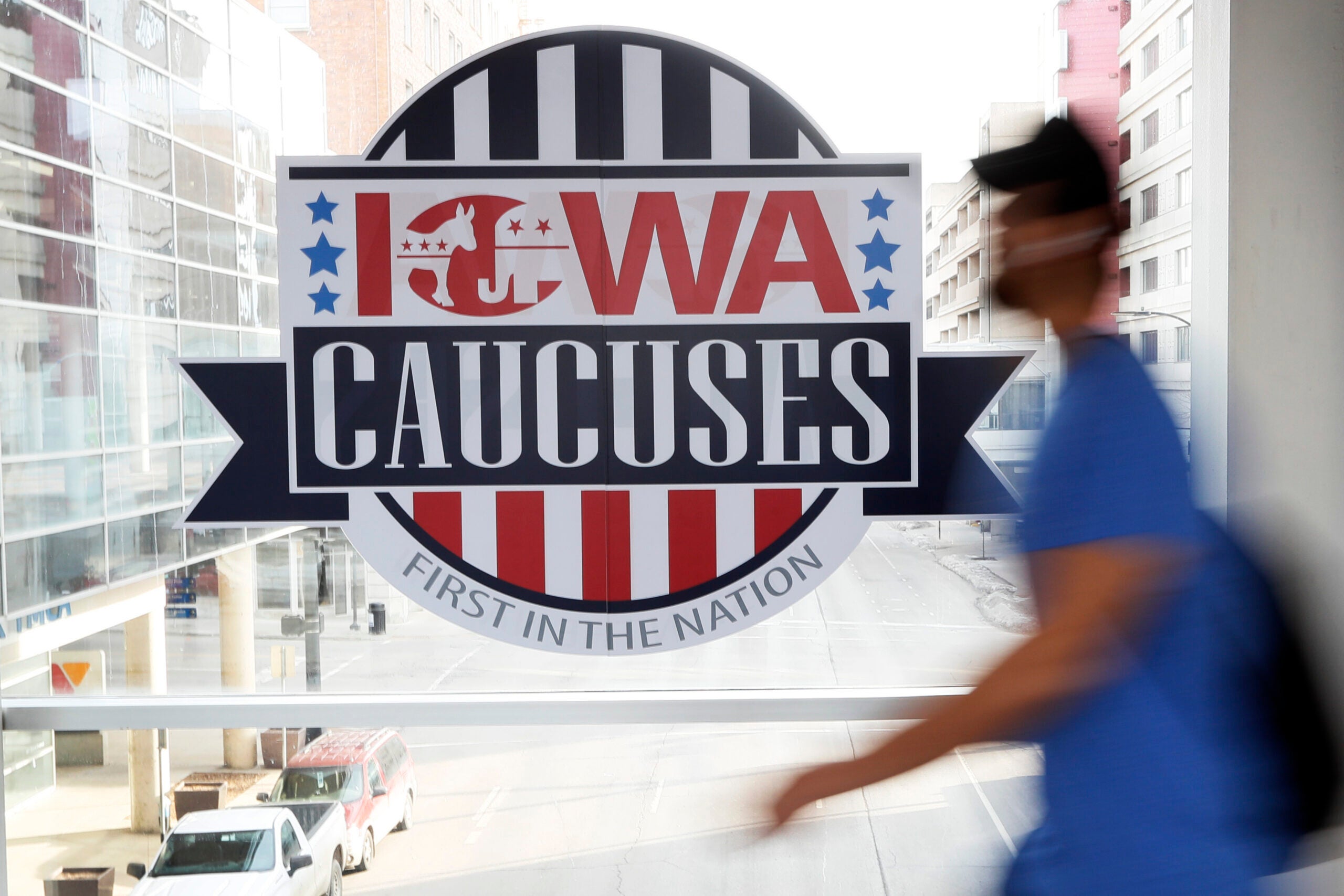 A pedestrian walks past a sign for the Iowa Caucuses on a Des Moines skywalk.