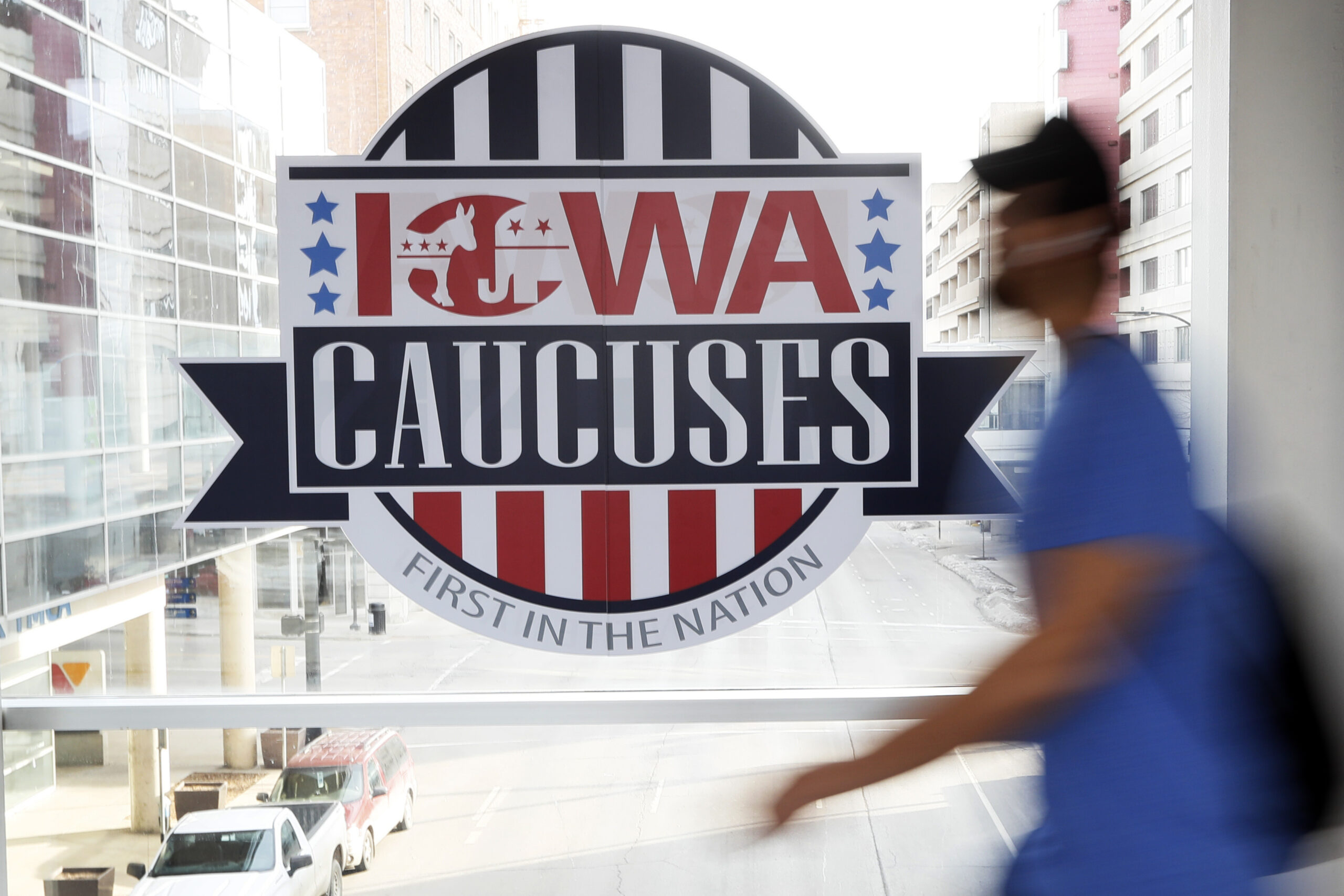 A pedestrian walks past a sign for the Iowa Caucuses on a Des Moines skywalk.