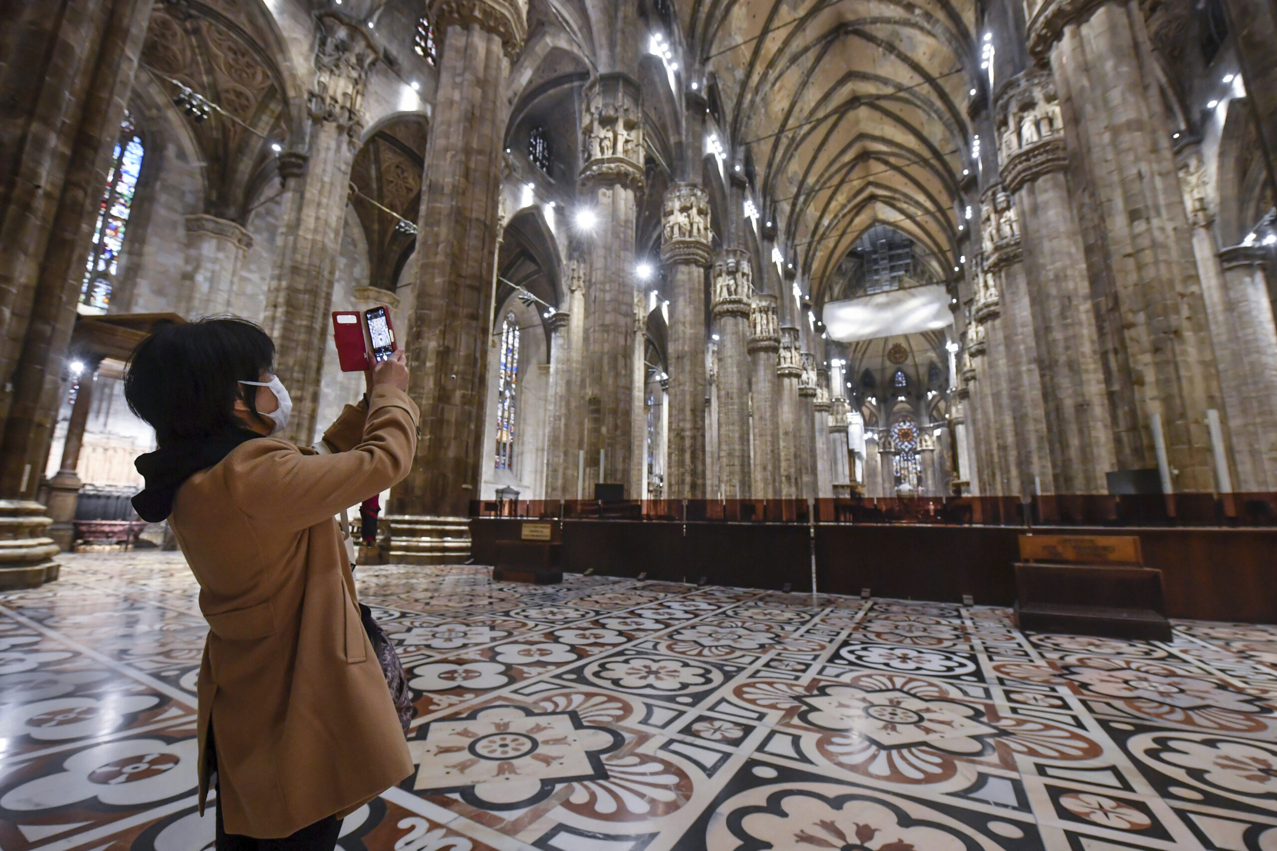 A tourist wearing a face mask takes pictures inside the Duomo gothic cathedral