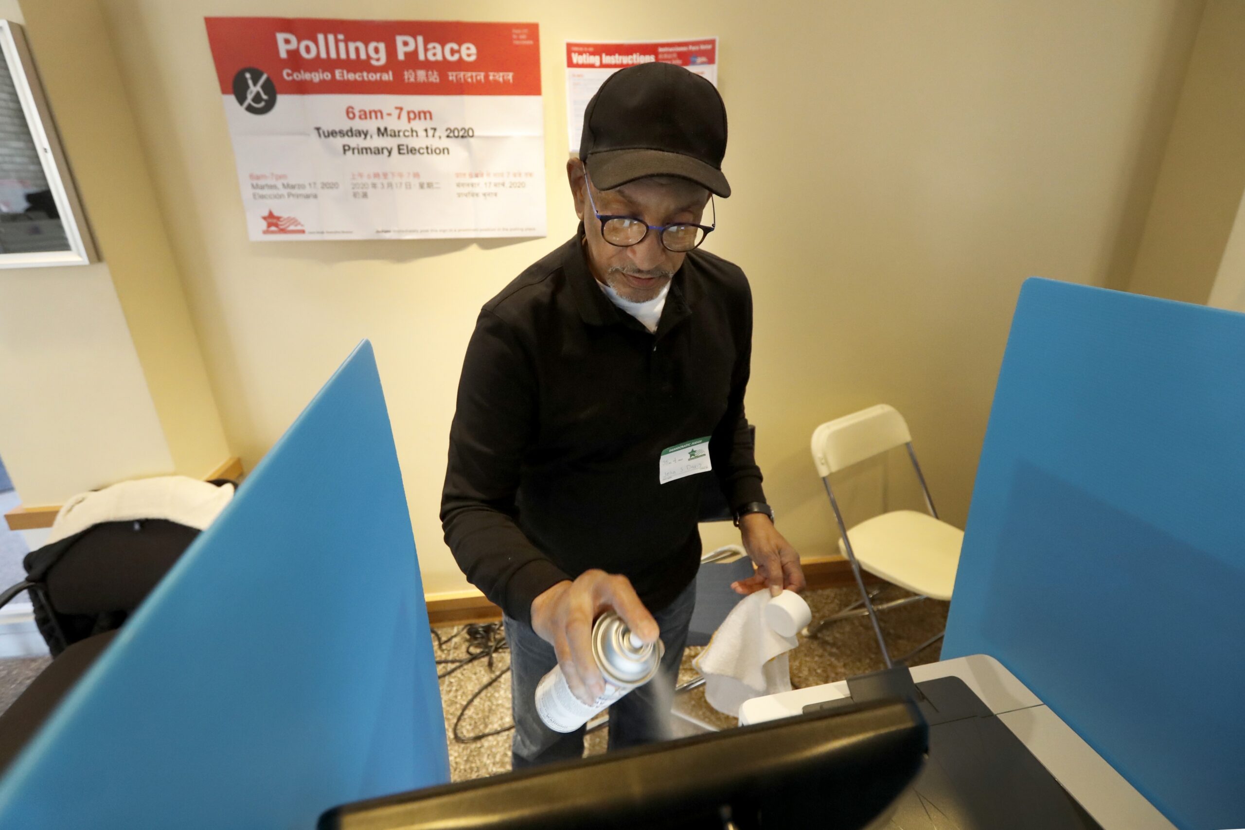 John Davis, a polling judge volunteer, sanitizes an electronic voting machine screen