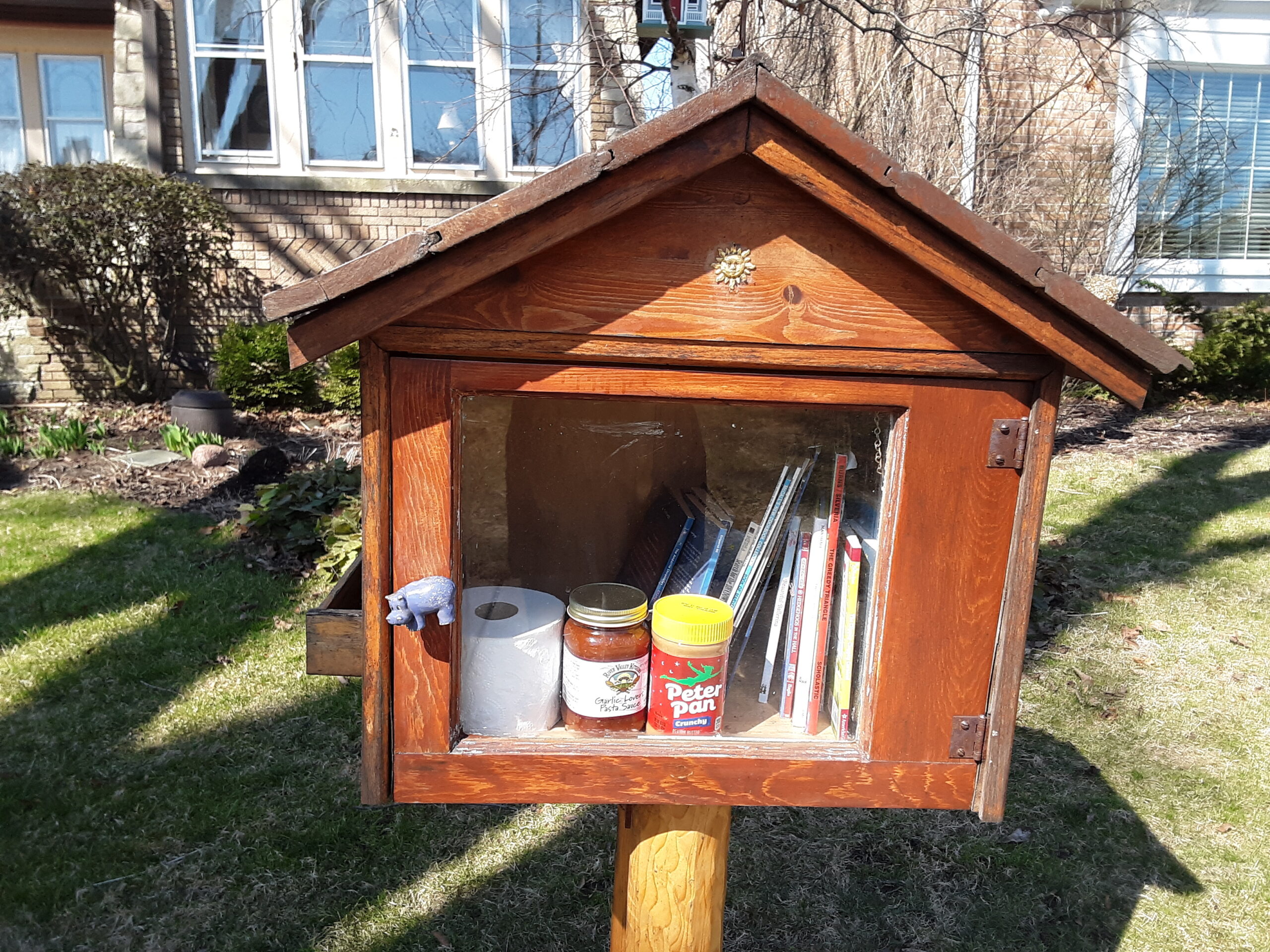 A Little Free Library with books, a roll of toilet paper, jar of spaghetti sauce, jar of peanut butter and chocolate, in Wauwatosa