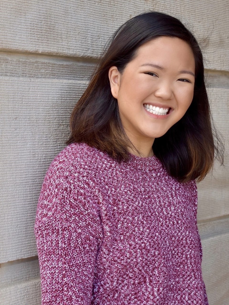 A young woman in a pink shirt smiles at the camera.