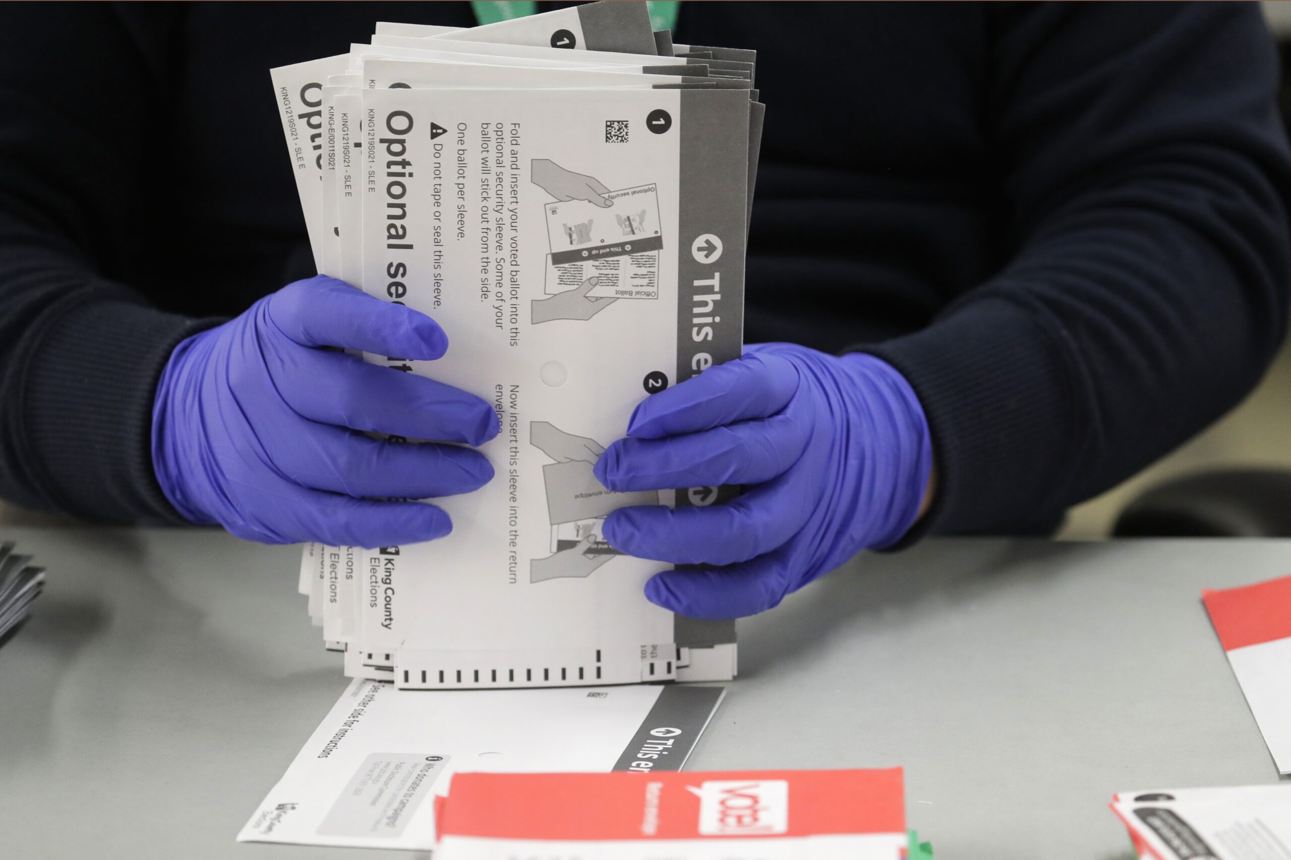 A worker wears gloves while handling ballots
