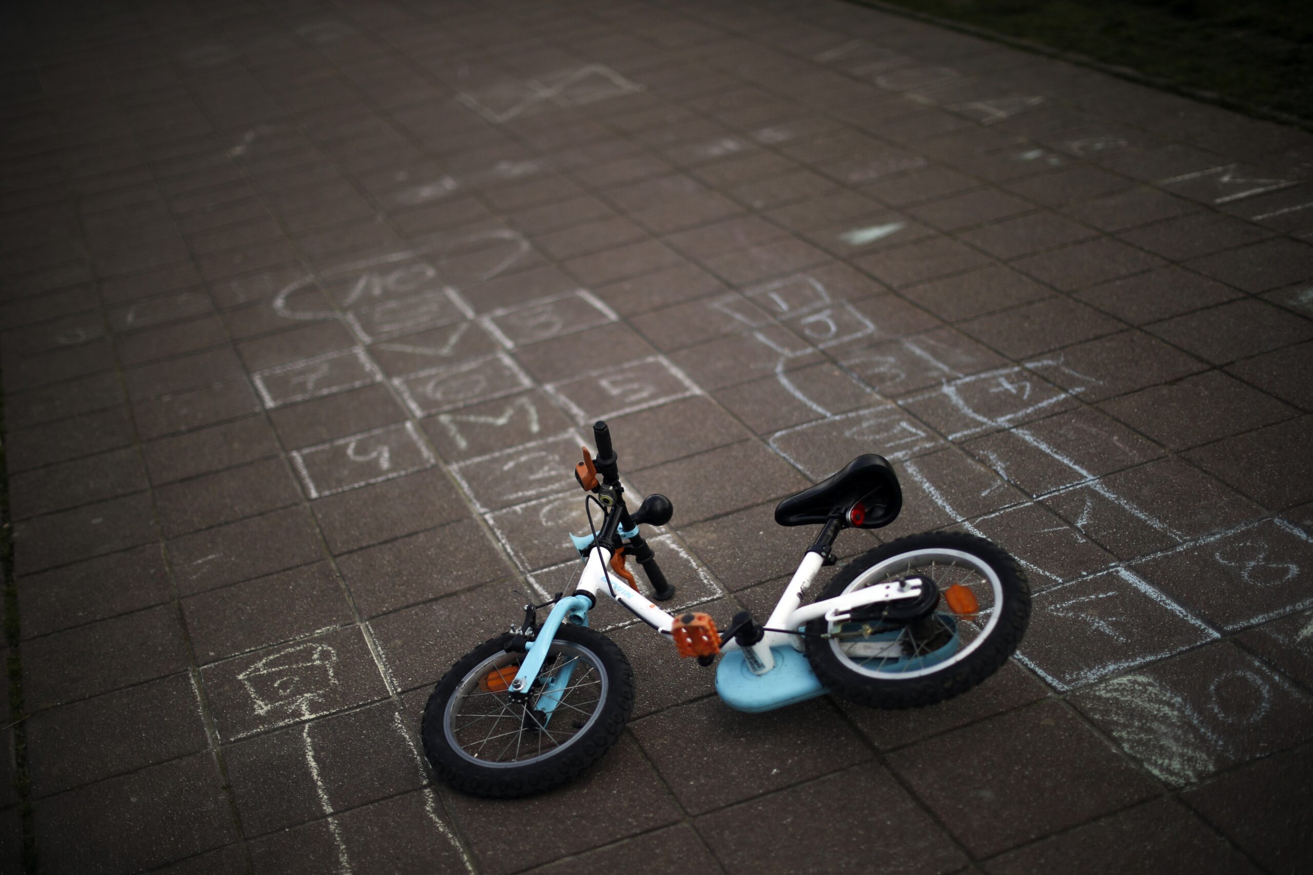 A child bicycle lies next to hopscotches sketched on the ground