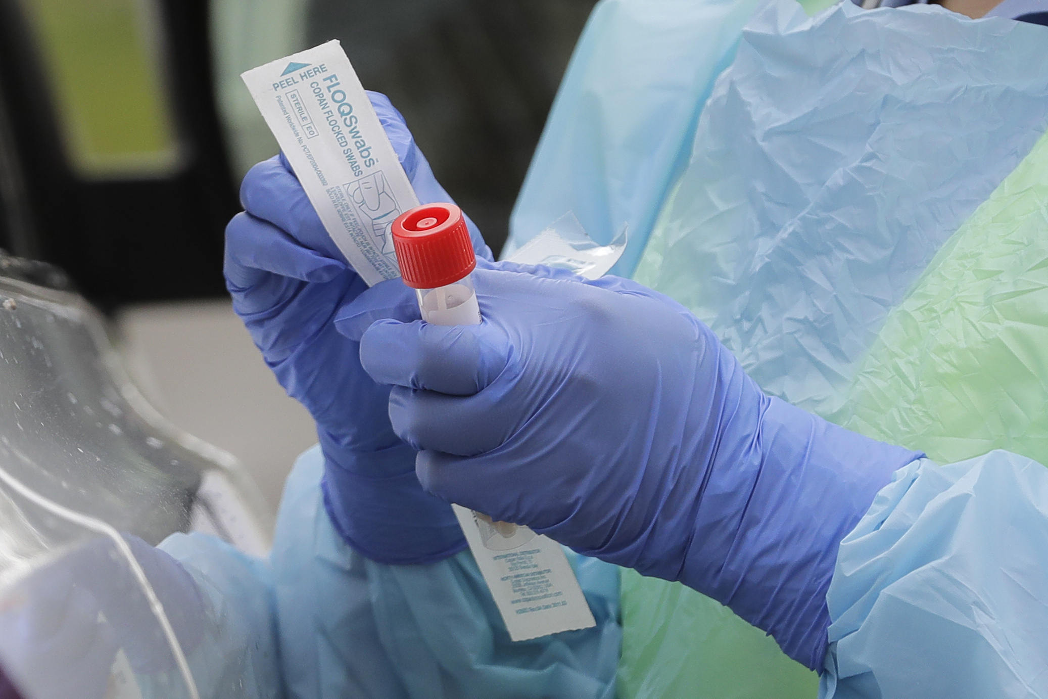 a nurse holds a vial and a swab at a drive-up coronavirus testing station