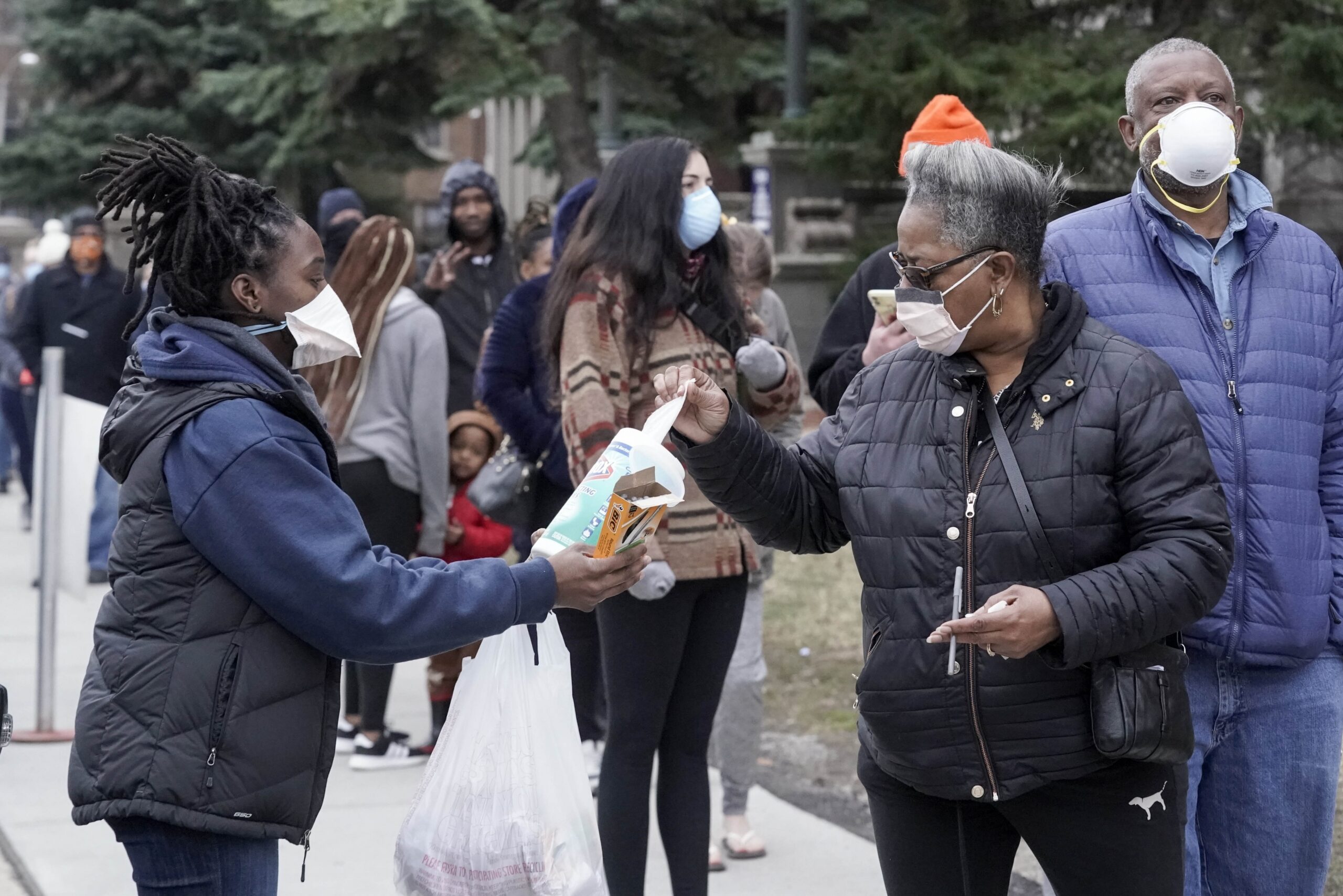 A worker hands out disinfectant wipes and pens as voters line up outside Riverside High School for Wisconsin's primary election