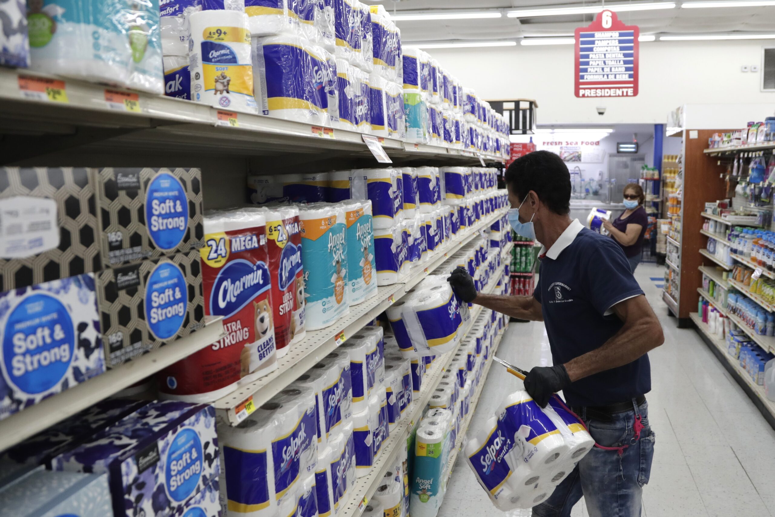 Jesus Padron wears a protective mask as he stocks shelves with toilet paper at the Presidente Supermarket