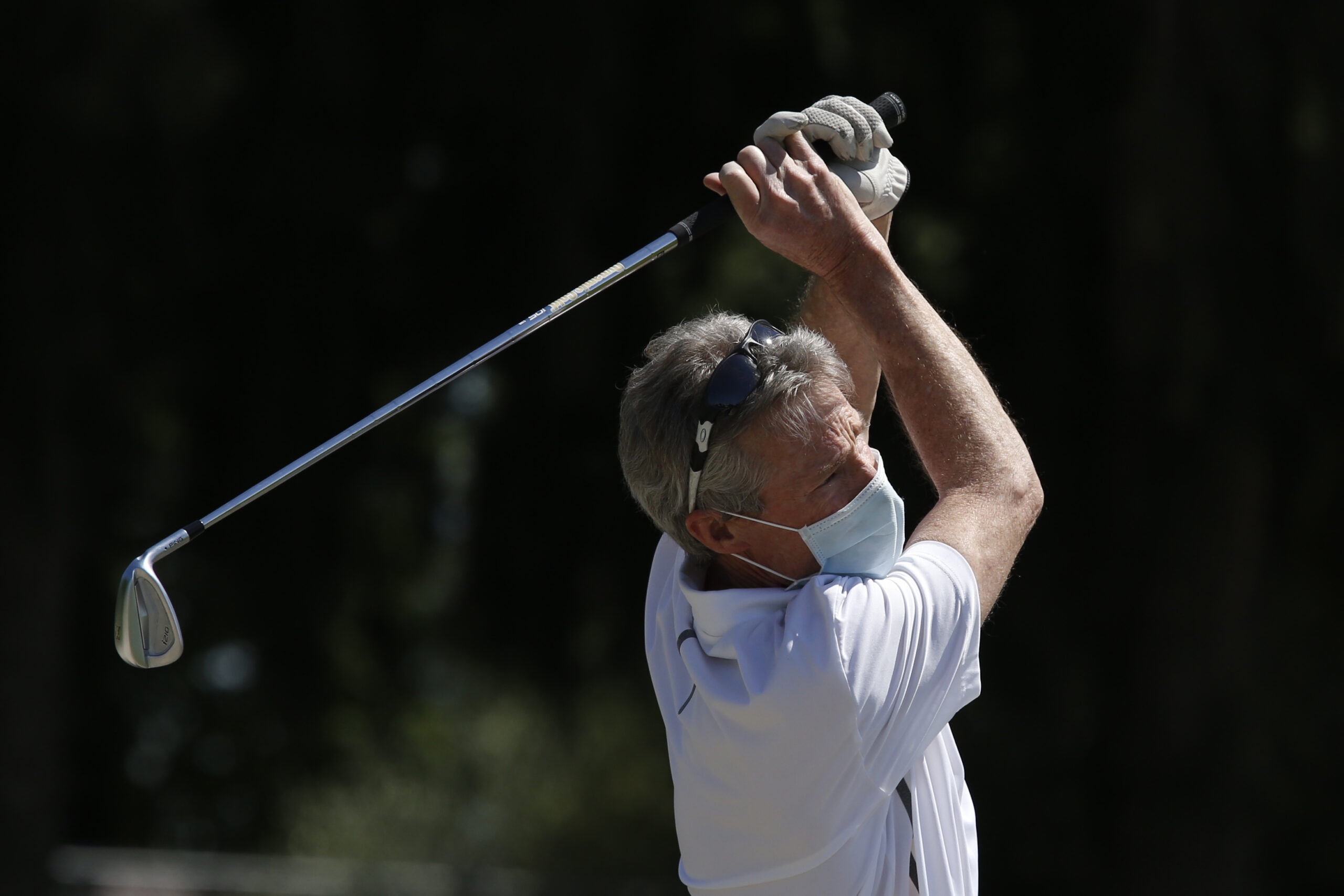 A golfer takes a practice swing while wearing a mask in California