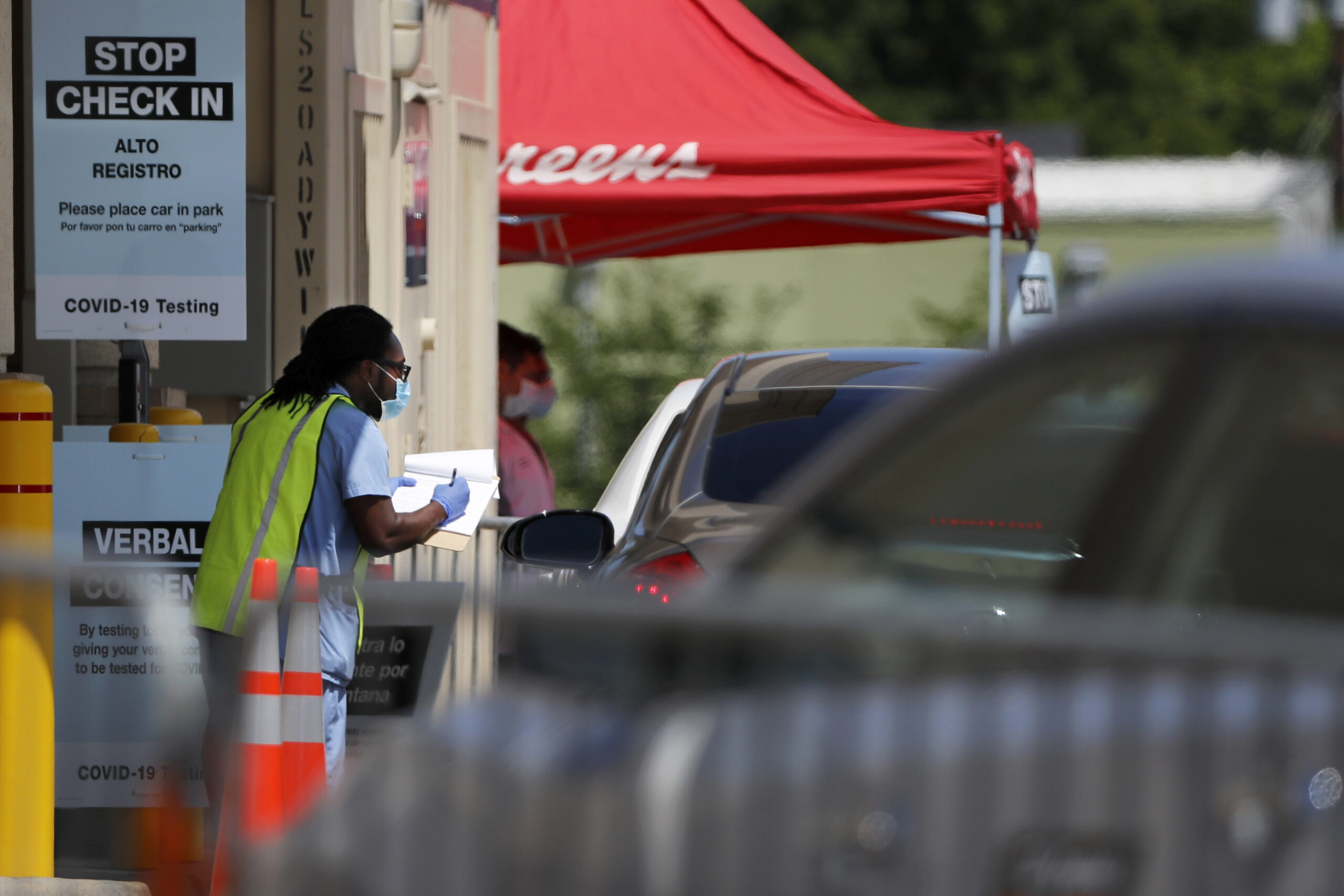 A slow but consistent flow of vehicles line up in a drive-thru area as a Walgreens pharmacist assists them with COVID-19 testing