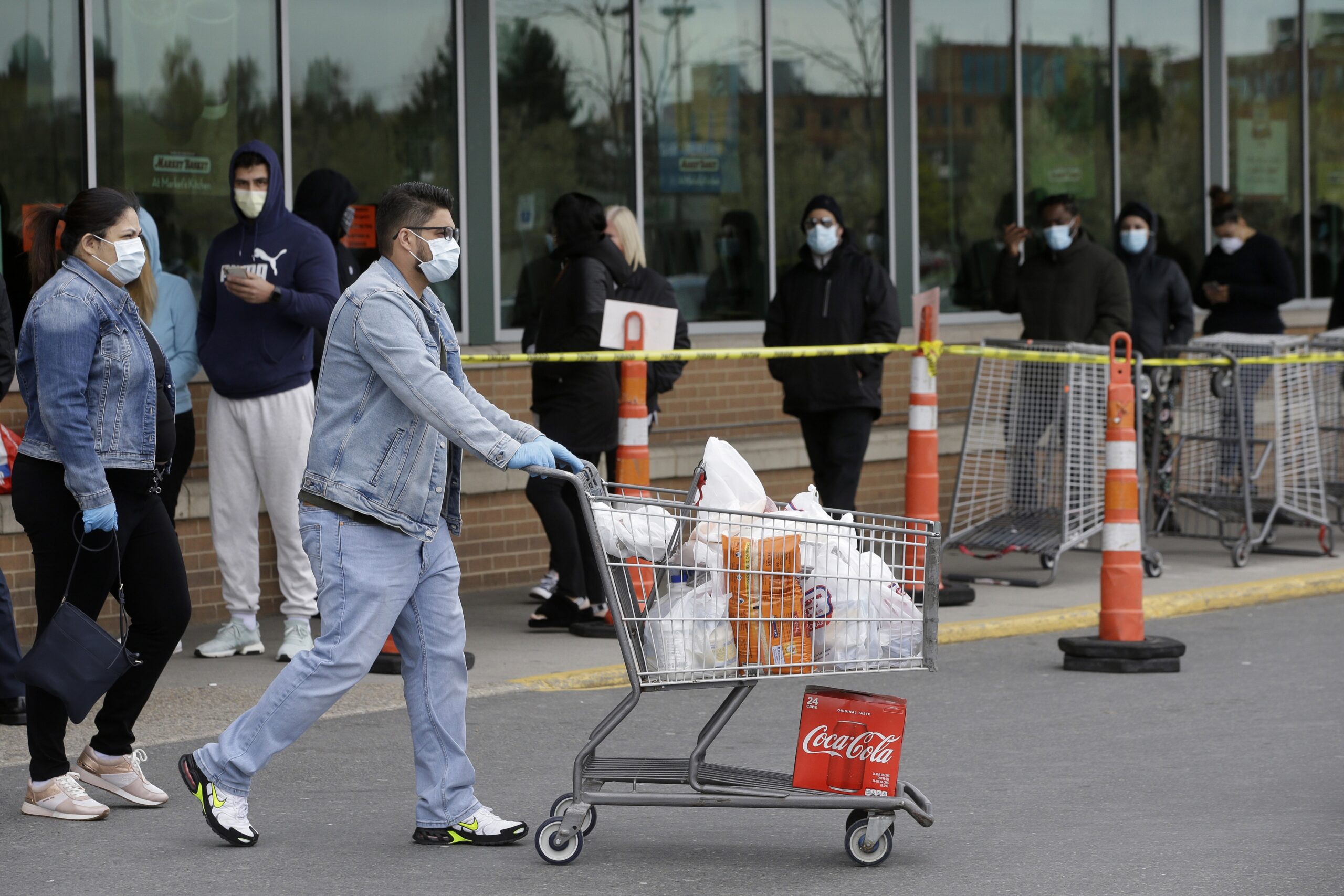 A man pushes a grocery cart while wearing a mask