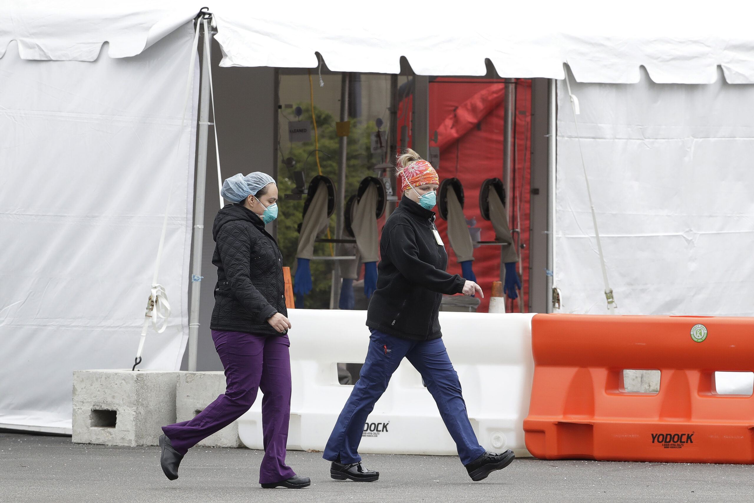 Women wearing masks walk past a tent at a coronavirus testing site