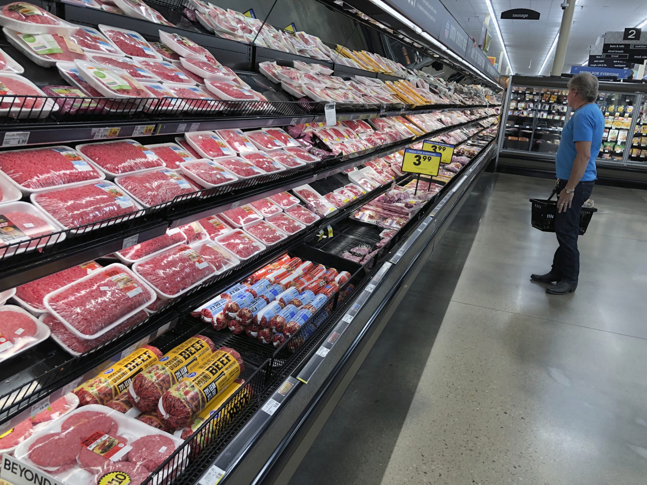A shopper surveys the overflowing selection of packaged meat in a grocery store