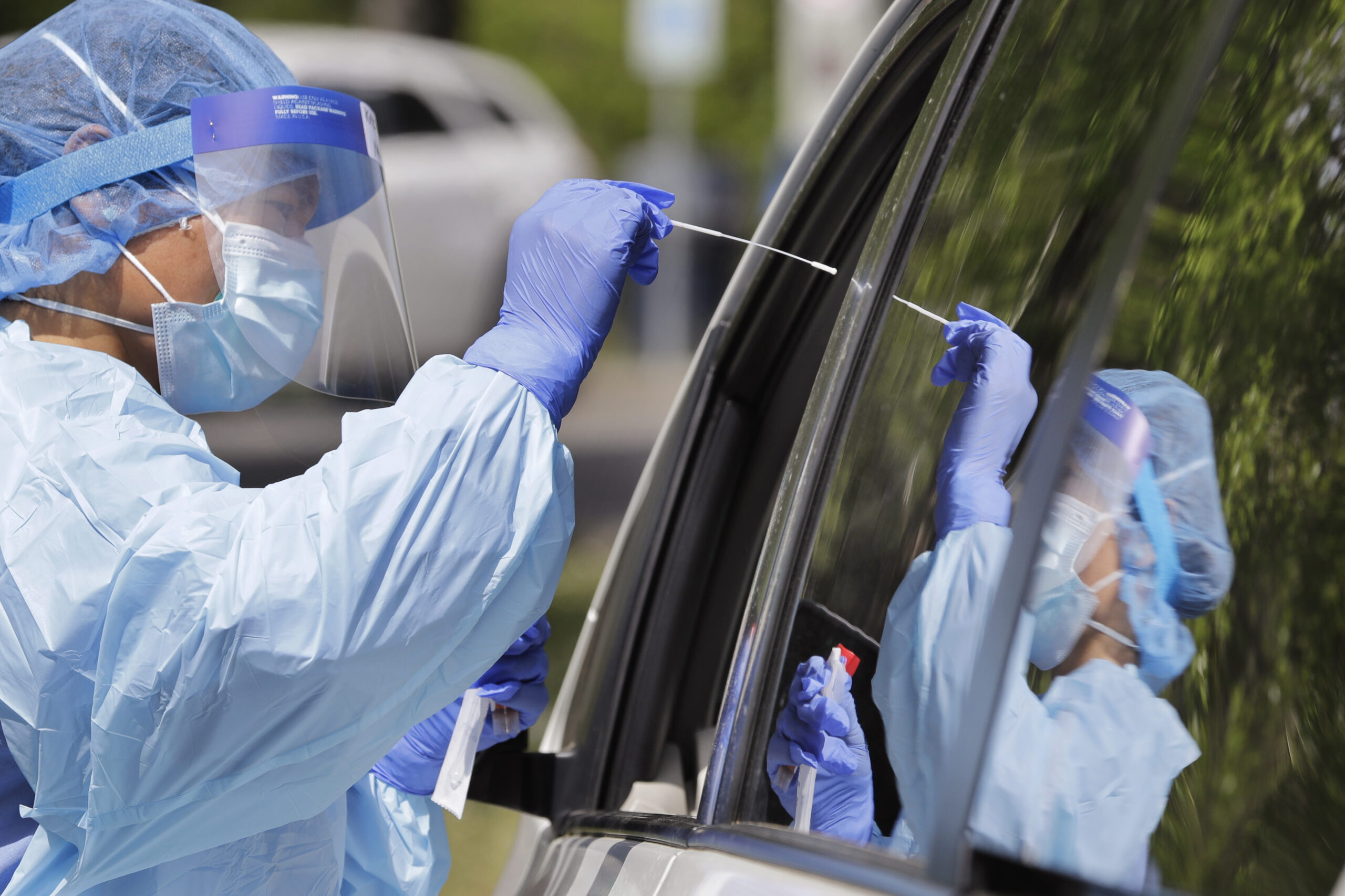 A medical assistant reaches in to take a nasal swab from a driver at a drive-up coronavirus testing site