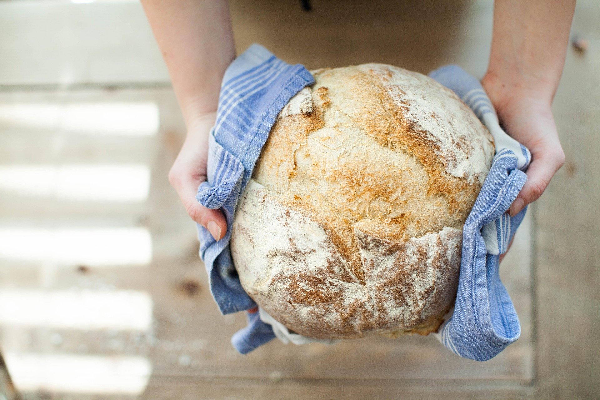 Hands holding loaf of fresh bread.