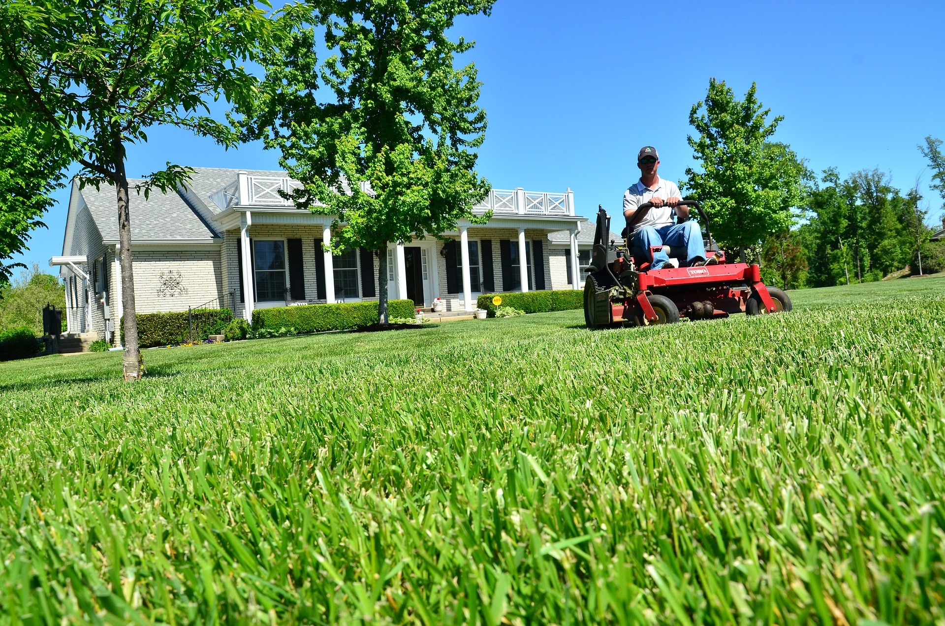 Cutting lawn on riding mower in front of house.
