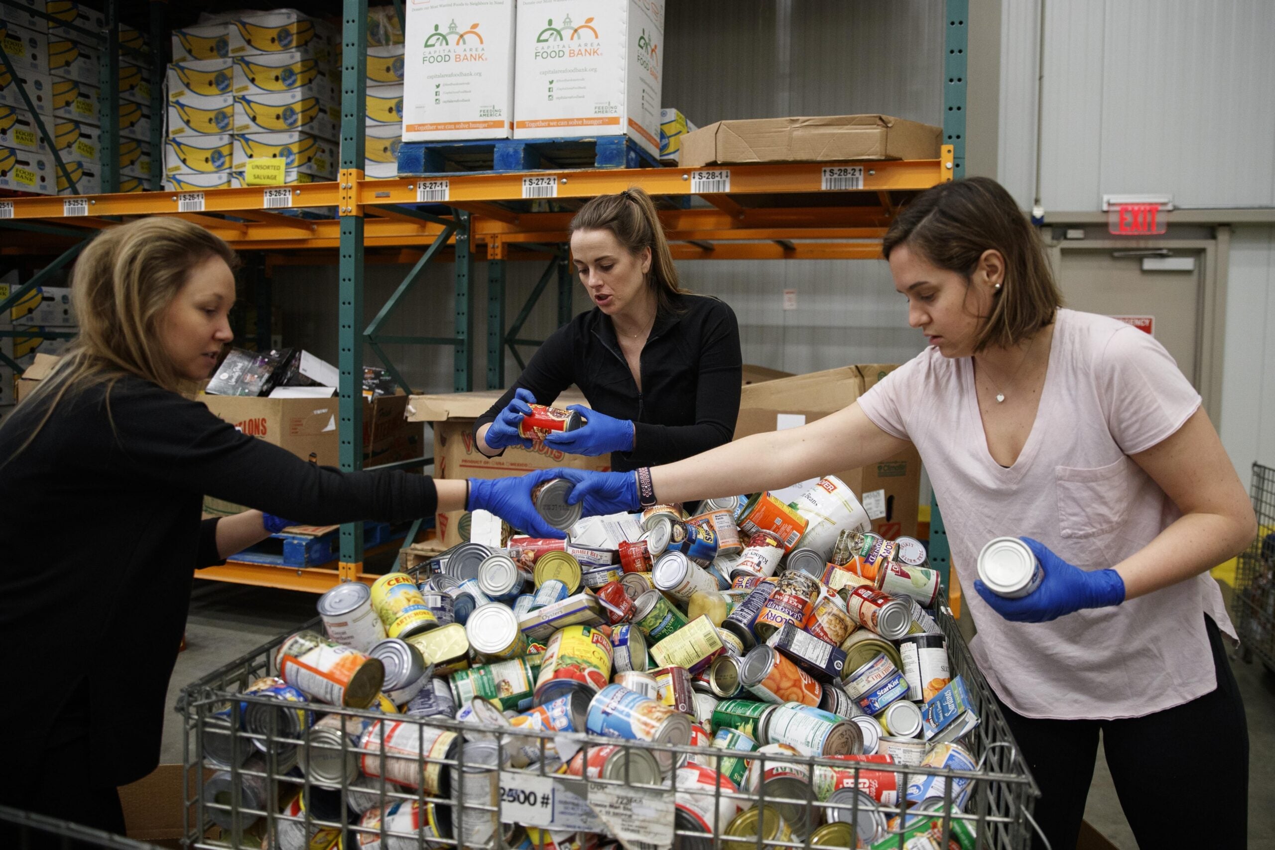 Katie Coerdt, Paige Dekker, and Caitlin Merely sort canned food as they wear disposable gloves at Capitol Area Food Bank
