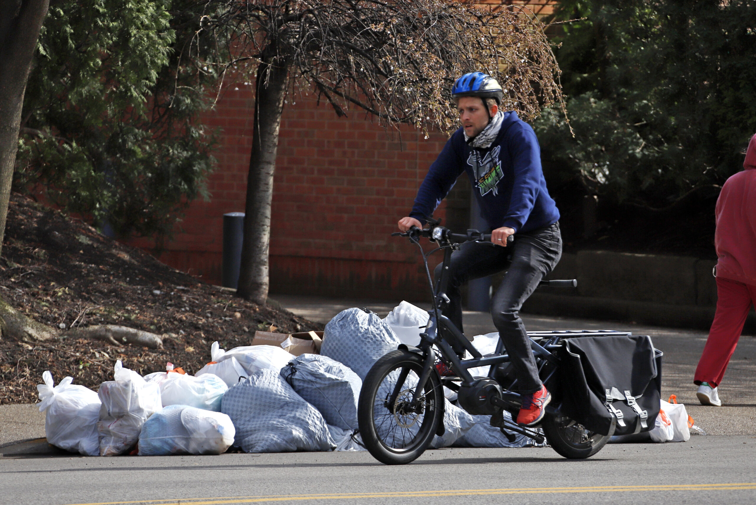 A bicyclist passes trash bags piled on the curb