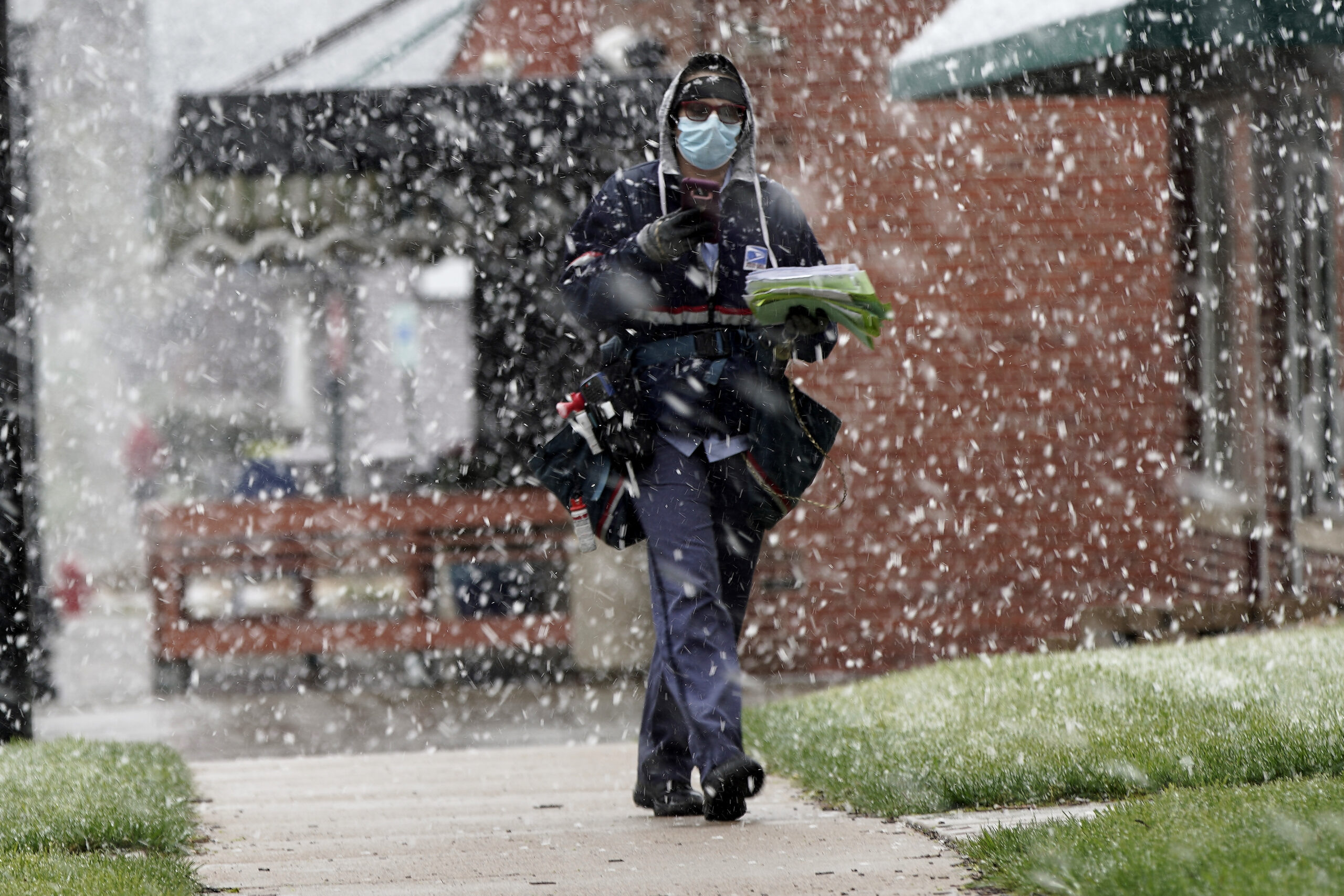 A USPS carrier wearing a face mask delivers mail in the snow
