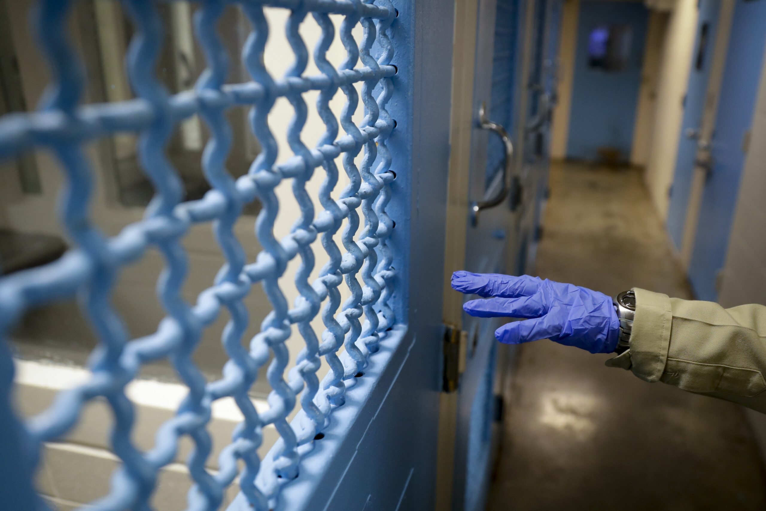 A gloved hand points to a holding cell at the hospital ward of a jail