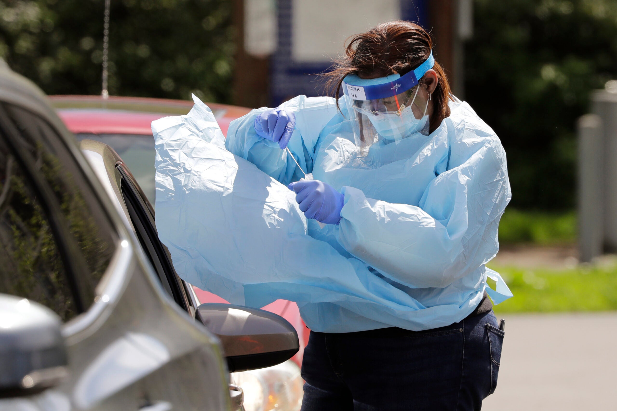 A medical assistant reaches in to take a nasal swab from a driver at a drive-up coronavirus testing site